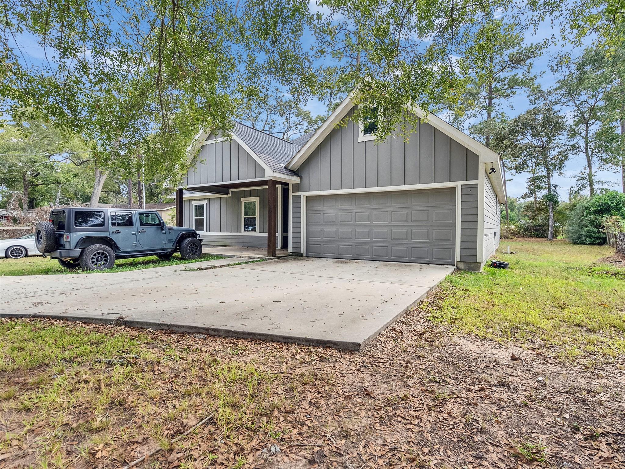 Gray house with a large two-car garage and broad driveway, partly shaded by mature trees.