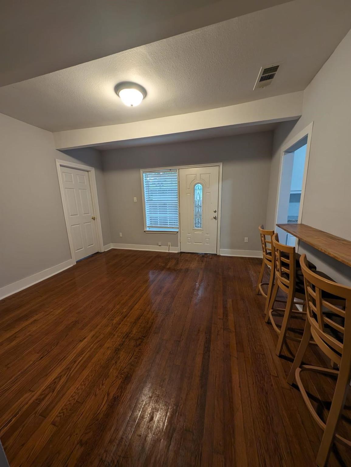 Entryway with polished hardwood floors, a glass-panel front door, and a counter with bar stools.