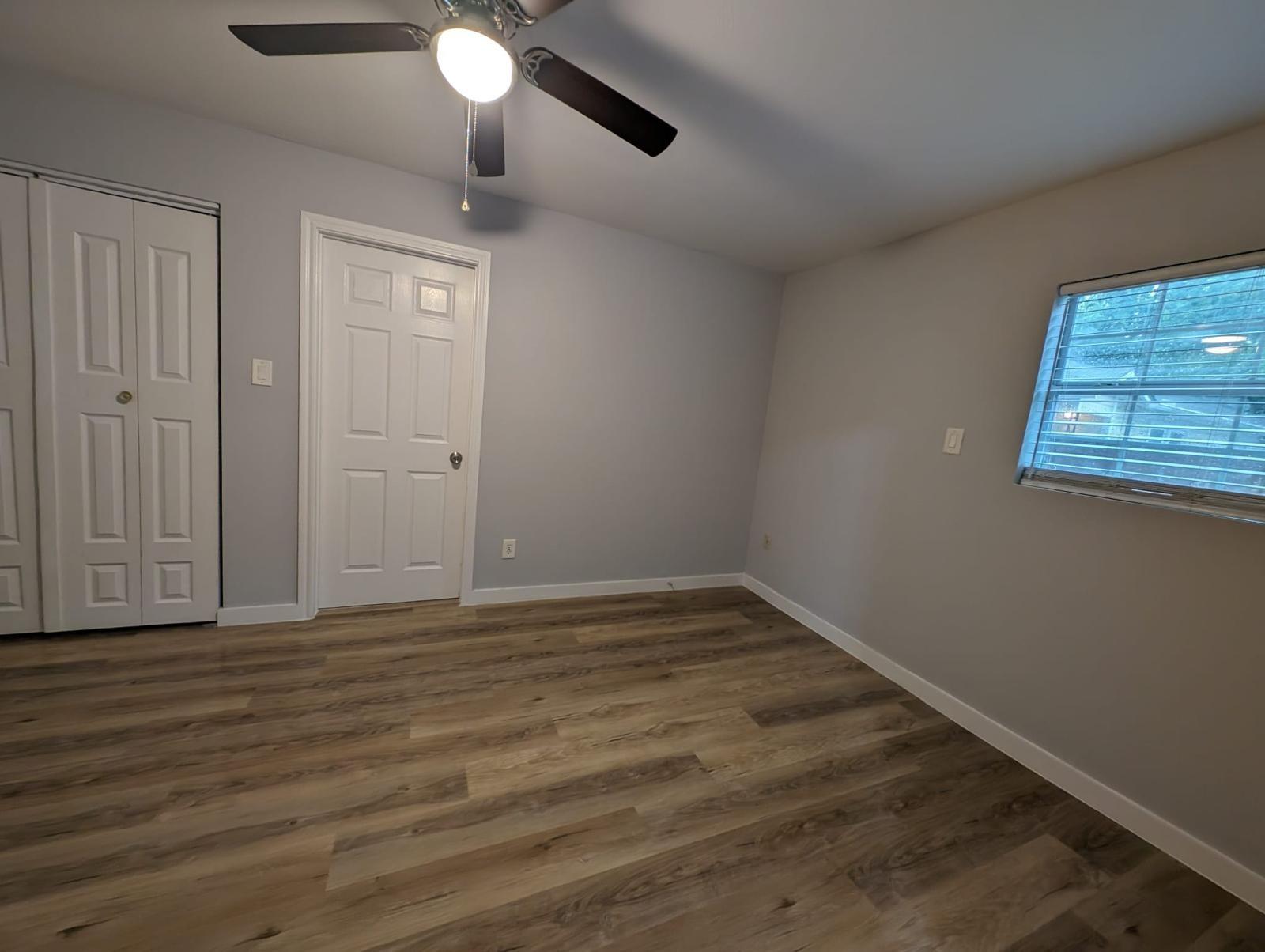 Empty bedroom with wood-look plank flooring, ceiling fan, double-door closet, and window blinds.
