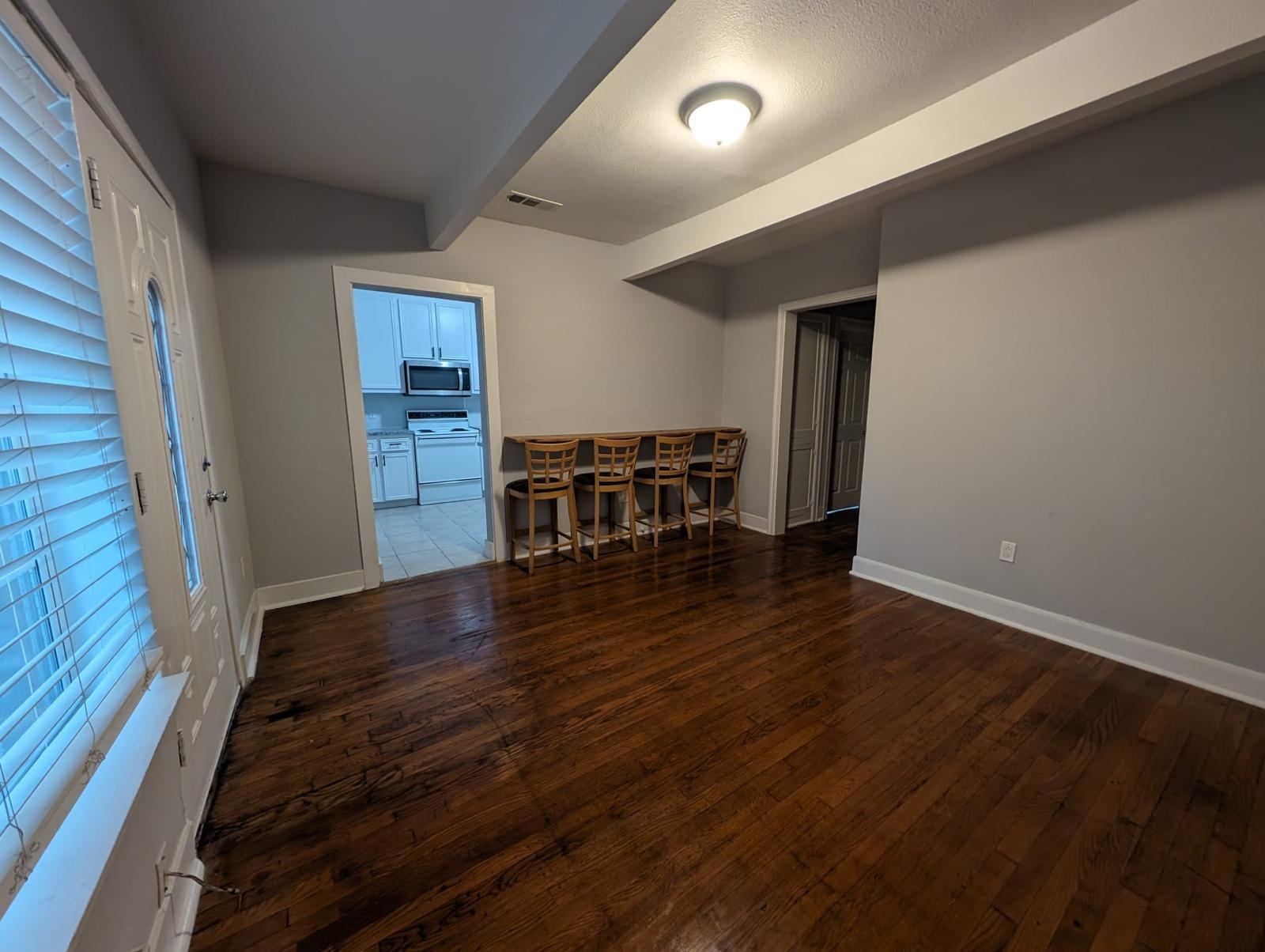 Dining area with dark hardwood floors and a counter with four wooden stools beside the kitchen doorway.