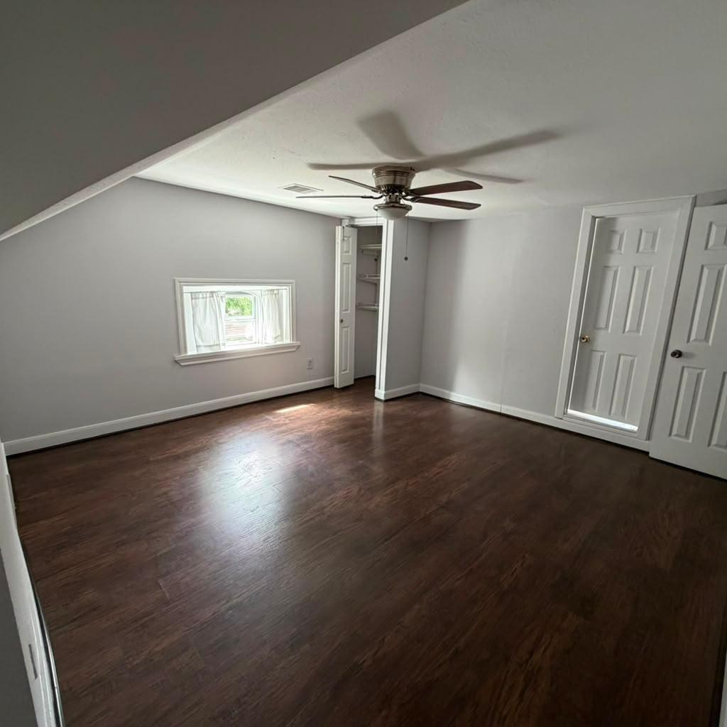 Empty bedroom with dark wood floors, a ceiling fan, and a small curtained window.