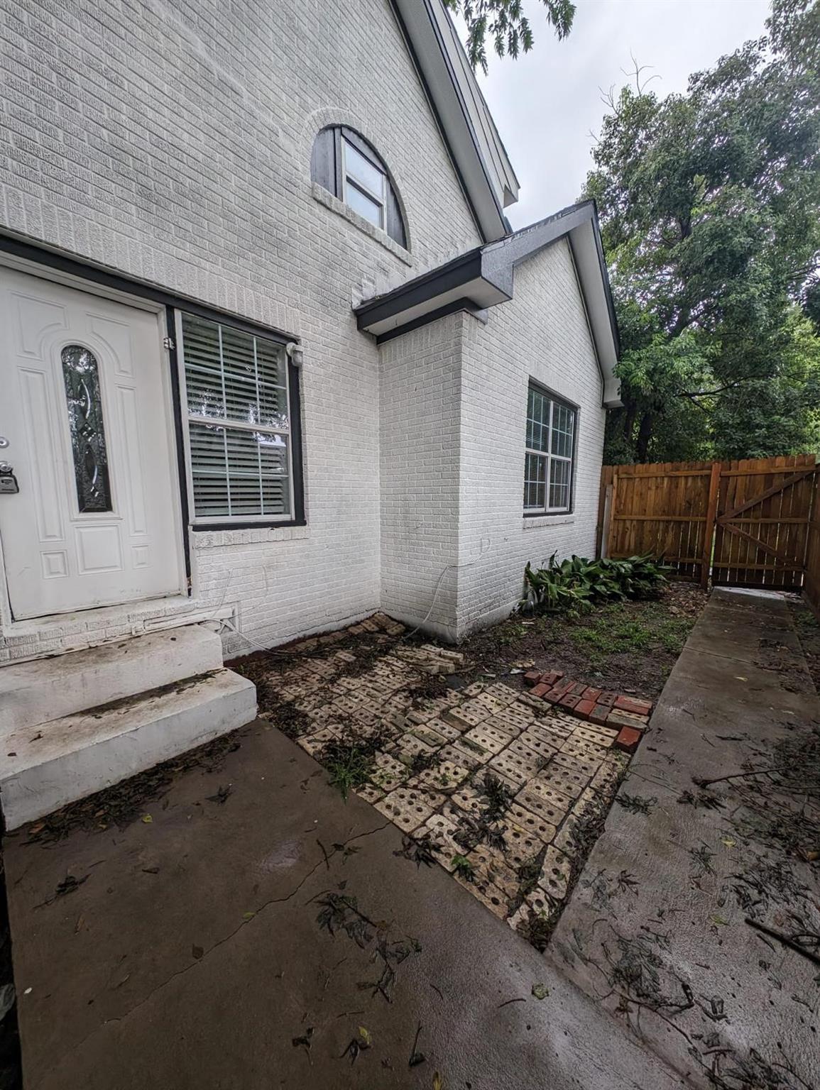 White brick house entry with an arched upper window and paved side walkway.
