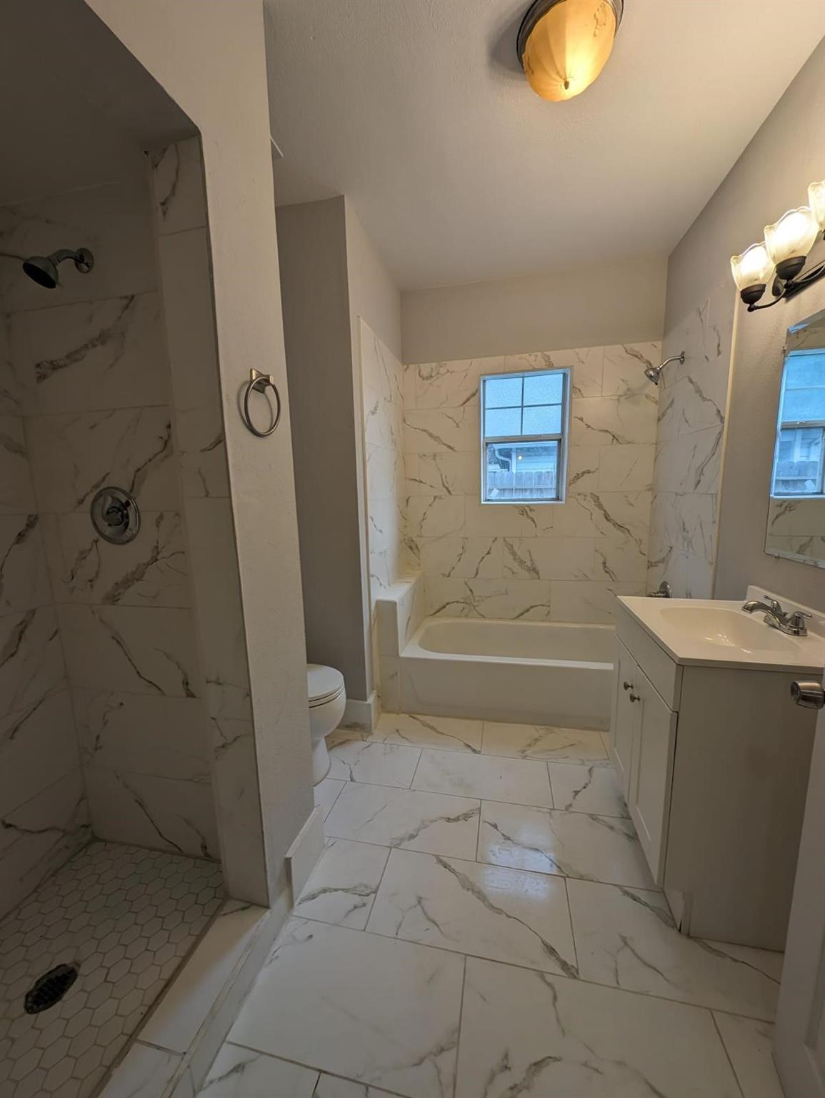 Bathroom with marble-look tile, a walk-in shower, bathtub beneath a window, and white vanity.