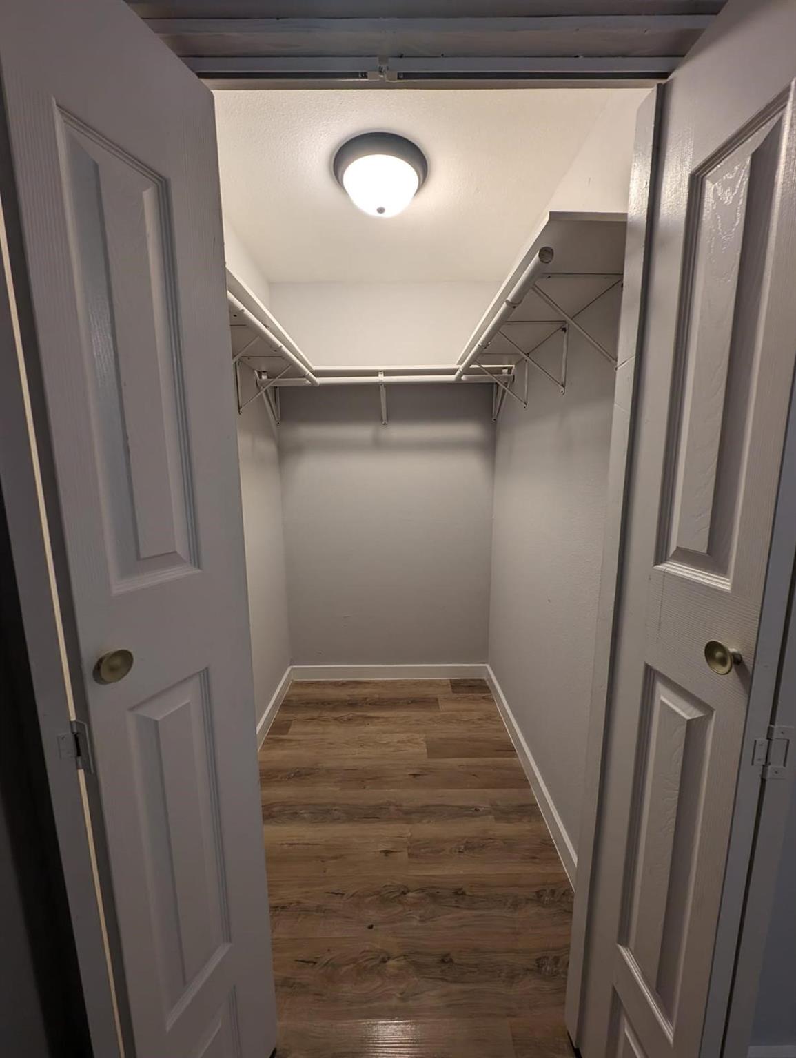 Empty walk-in closet with white shelving, hanging rods, and wood-look flooring.