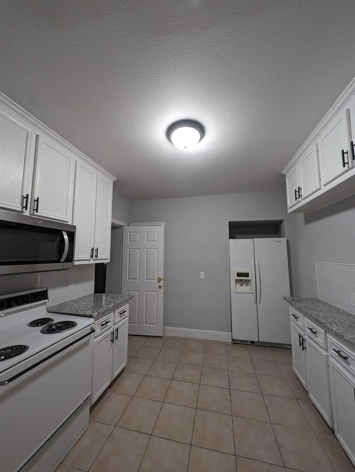 Kitchen with white cabinetry, granite counters, electric range, and side-by-side refrigerator.