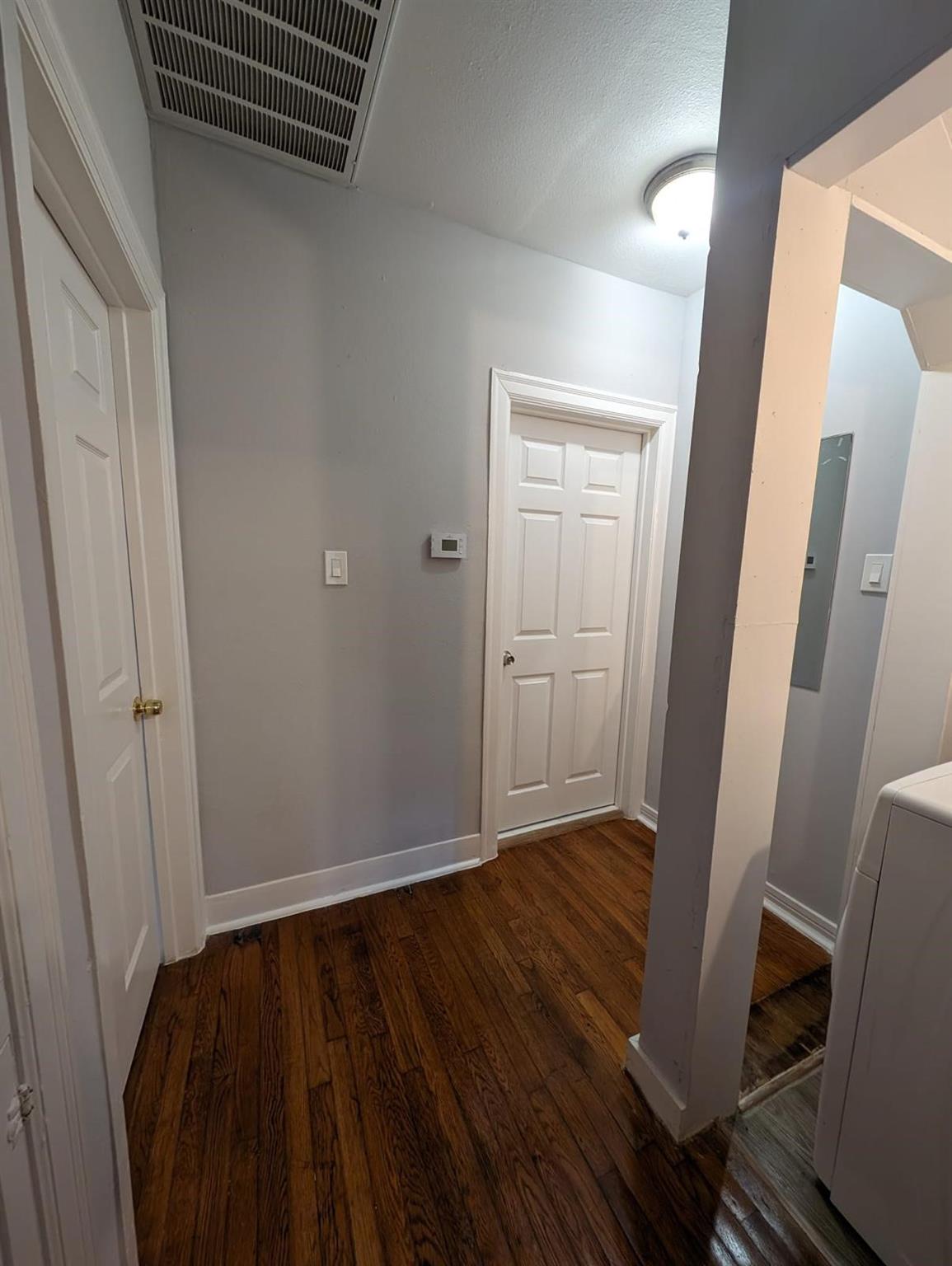Hallway with dark wood floors, gray walls, white paneled doors, and a washer or dryer at the right edge.