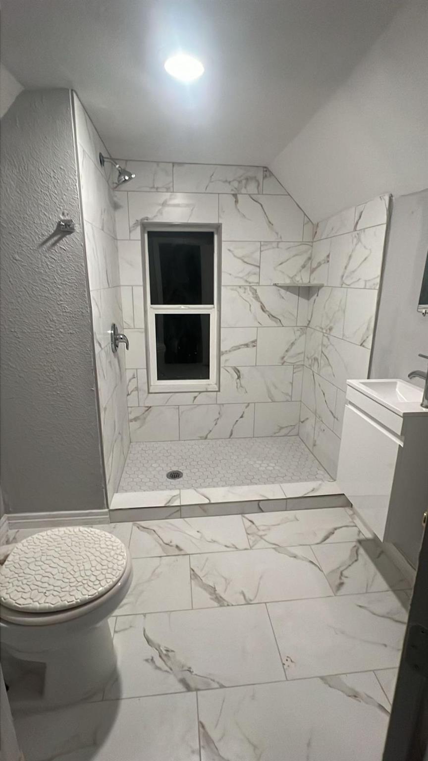 Bathroom with a marble-look tiled walk-in shower and window.