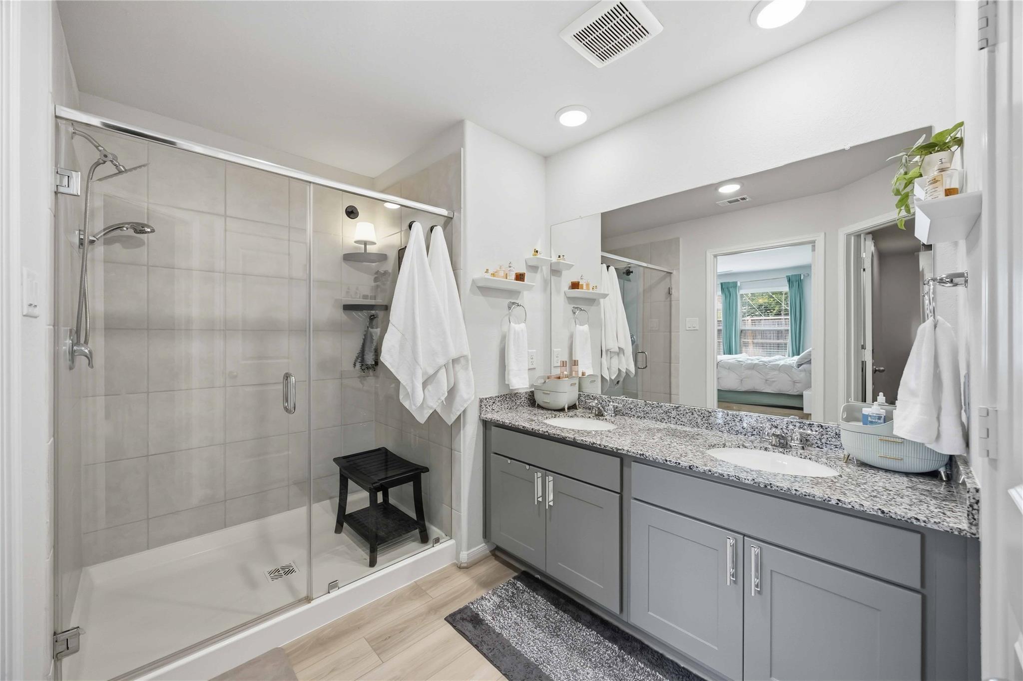 Bathroom with glass walk-in shower and gray double vanity topped with granite.