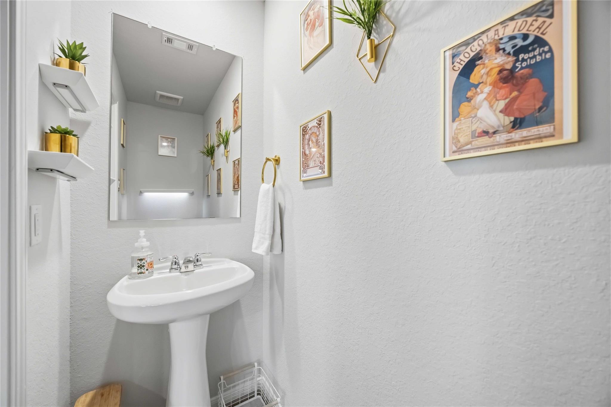 Bathroom sink with a large mirror, gold towel ring, and framed artwork.