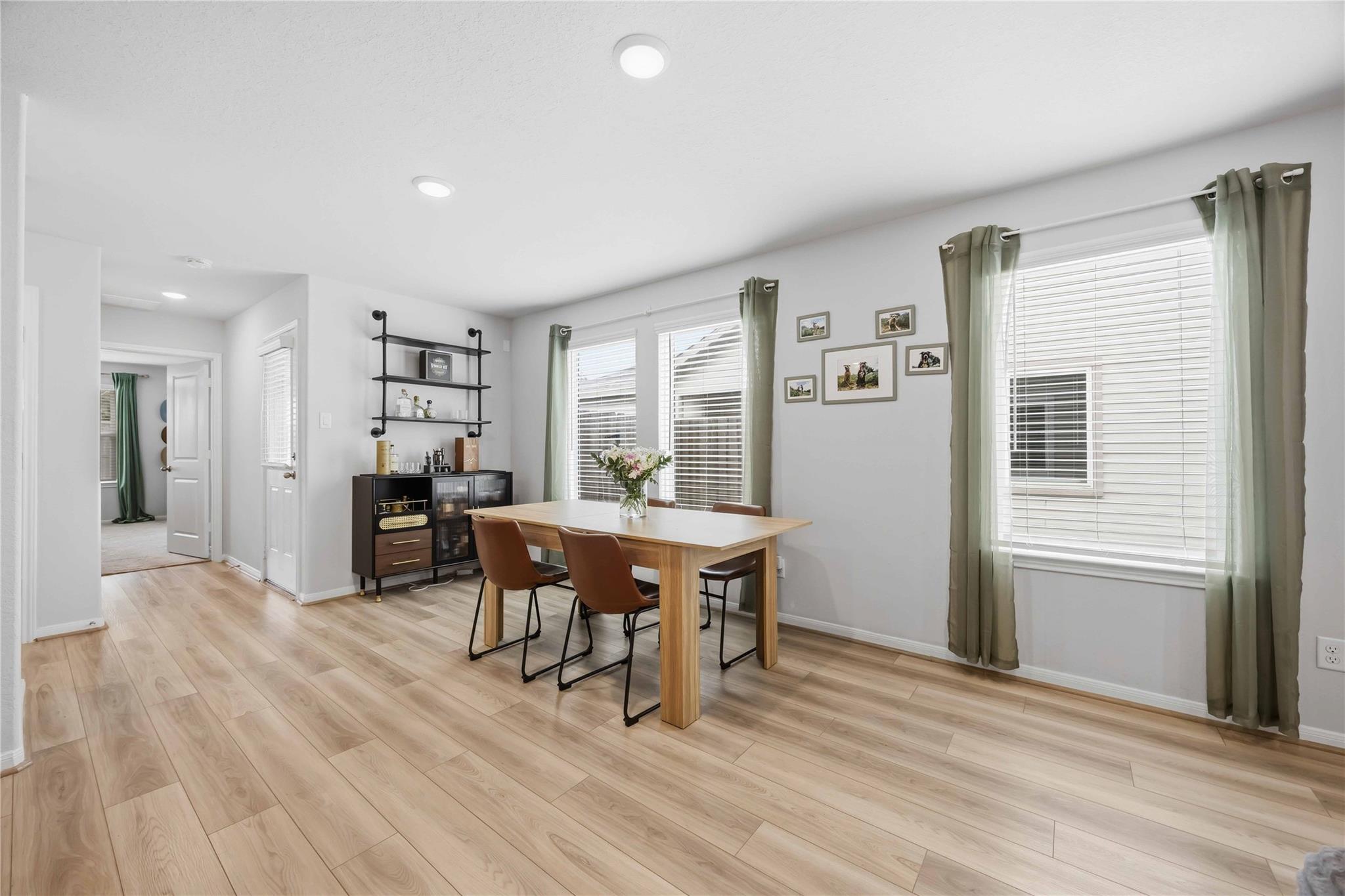 Dining room with a light wood table, brown chairs, green curtains, and pale wood-look flooring.