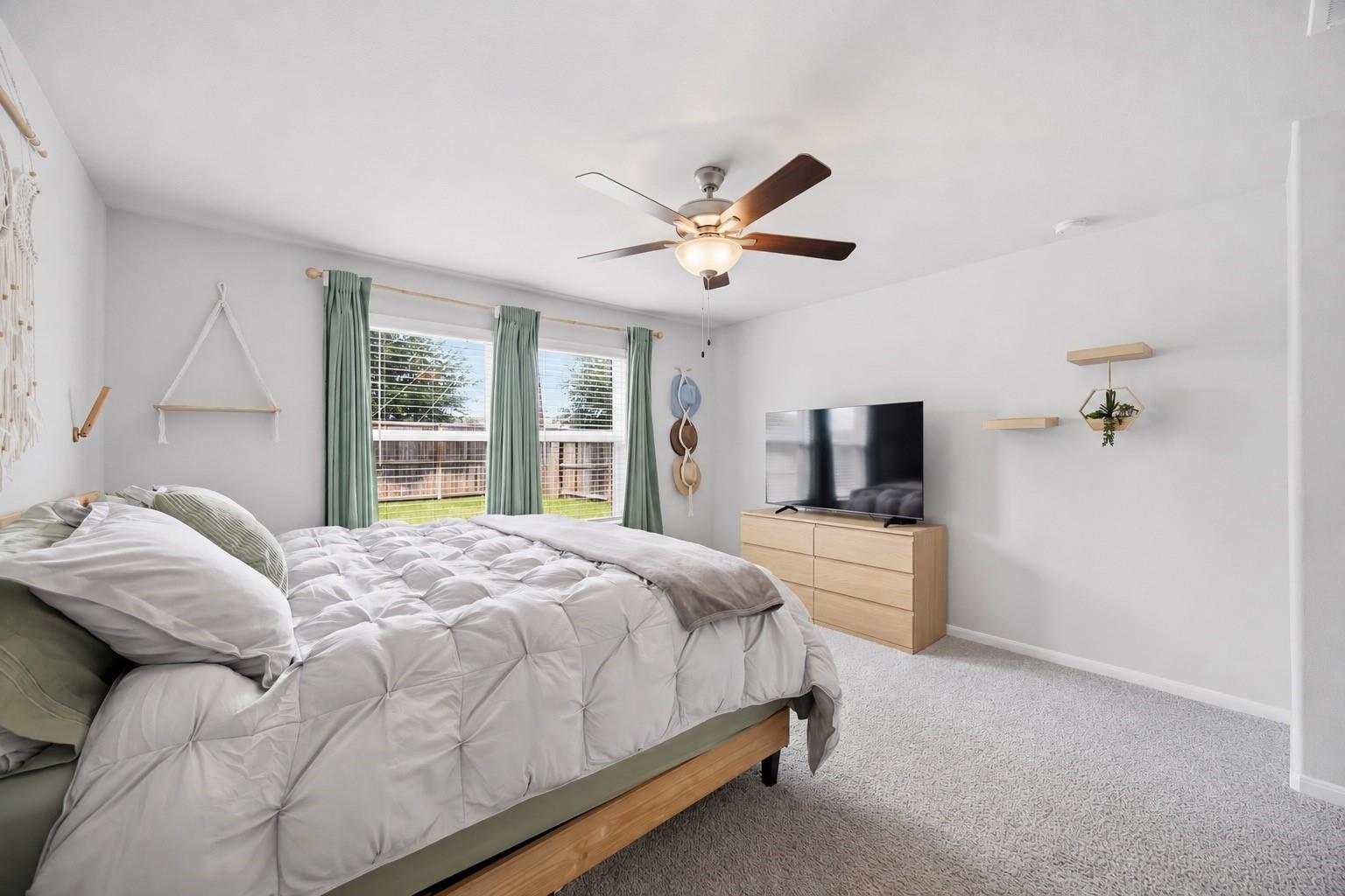Bedroom with white bedding, green window curtains, and a television on a light wood dresser.