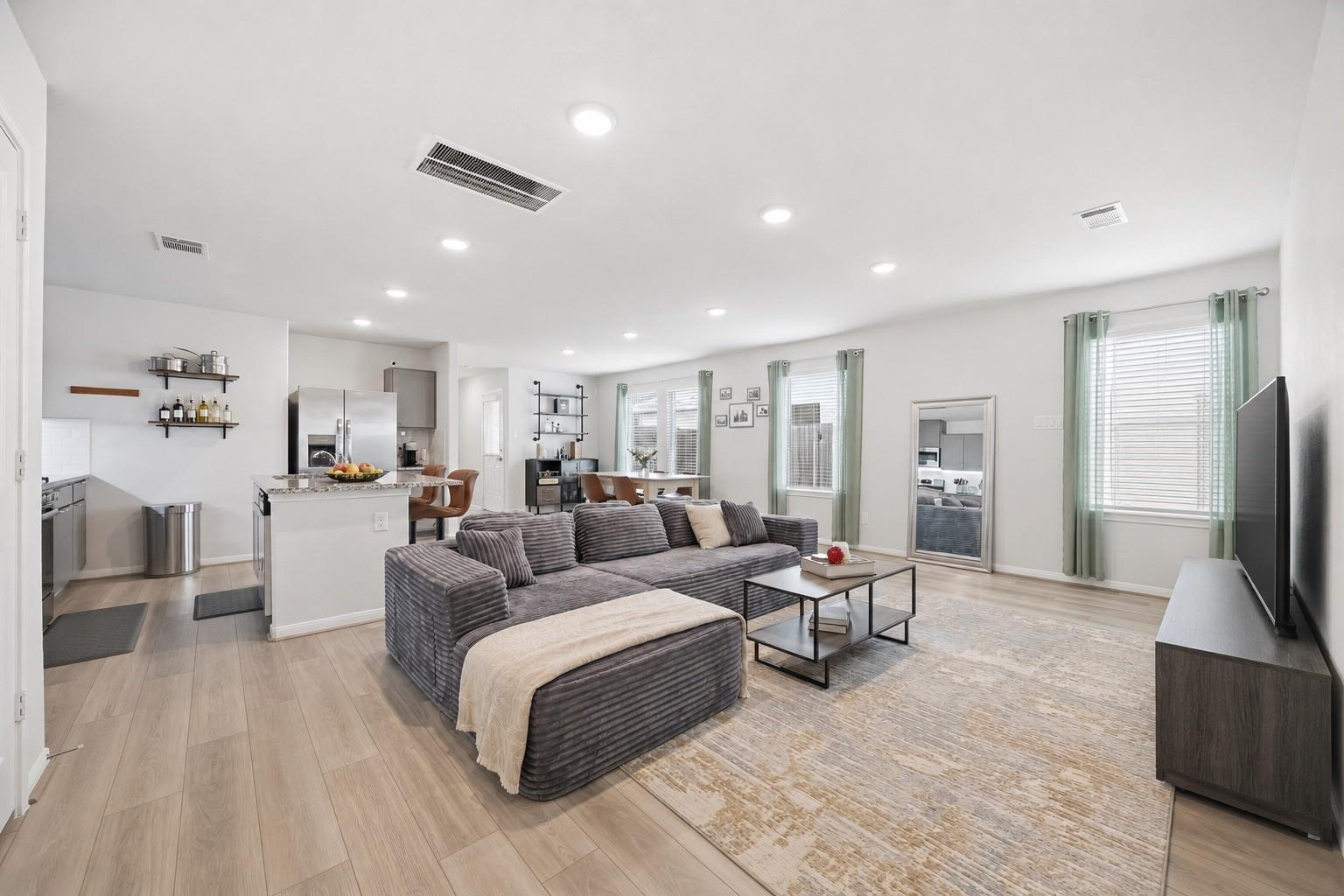 Open-plan living room with a gray sectional, large rug, and adjoining kitchen and dining area.