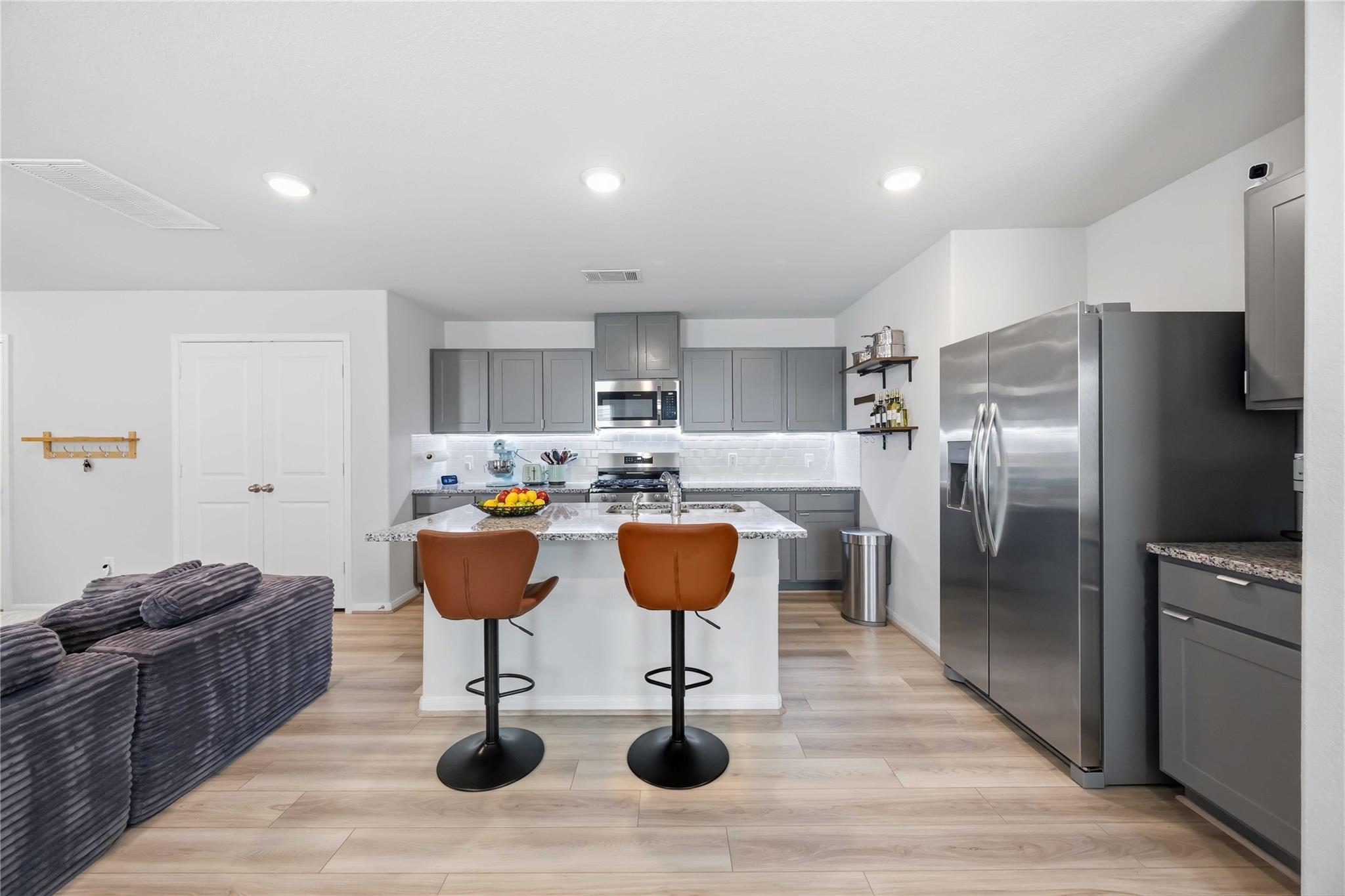 Modern kitchen with gray cabinets, stainless steel appliances, and an island with two brown bar stools.