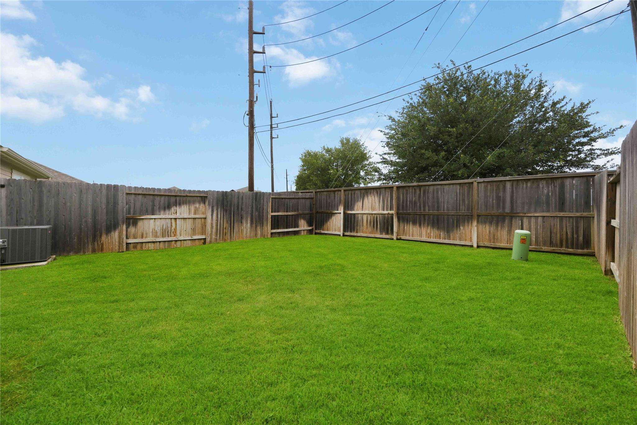 Fenced backyard with a wide green lawn, mature tree, and overhead utility wires.