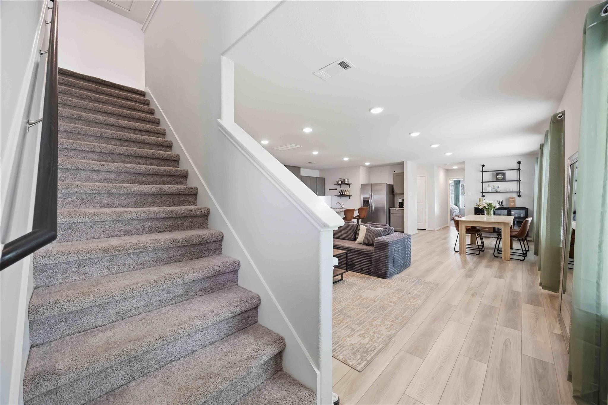 Open-plan home interior with a carpeted staircase beside the living and dining areas.