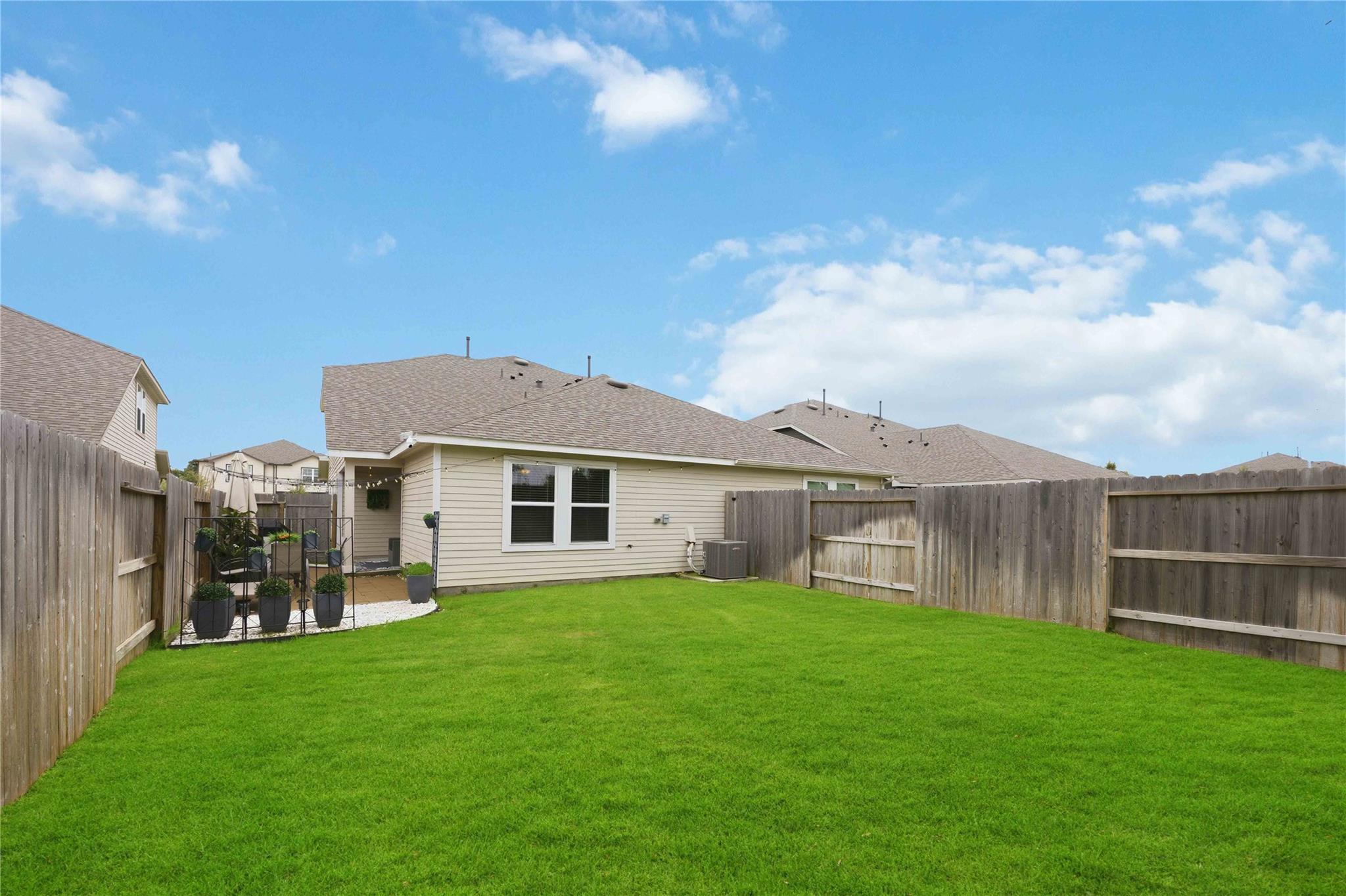 Fenced backyard with a broad green lawn and a small patio seating area beside the house.