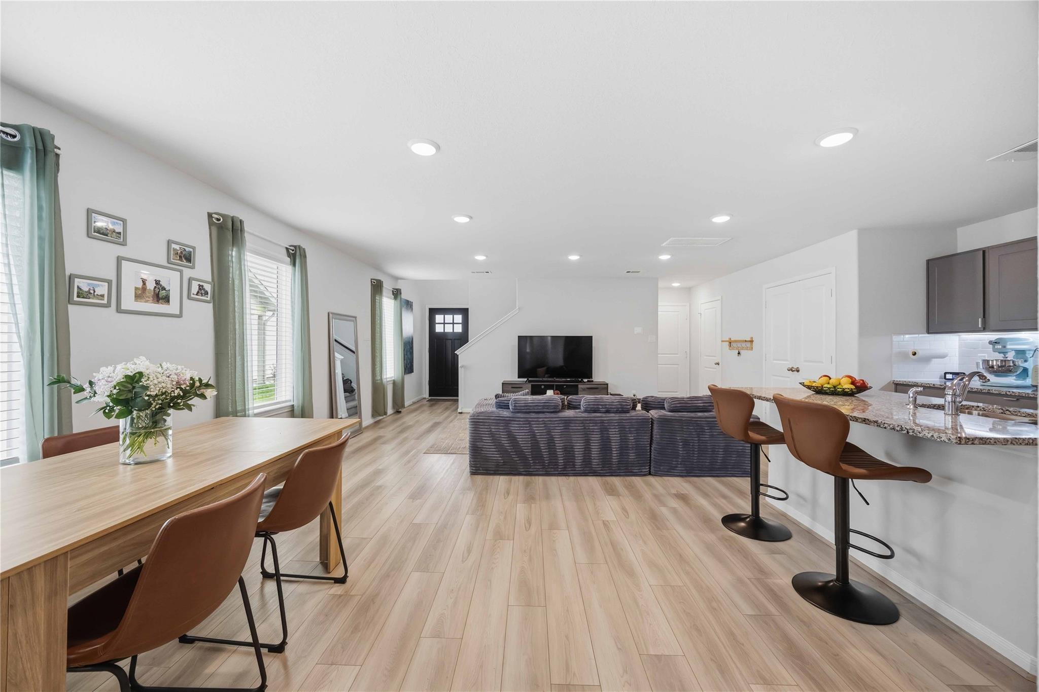 Open-plan living and dining area with a sectional sofa, window-side table, and kitchen island with bar seating.