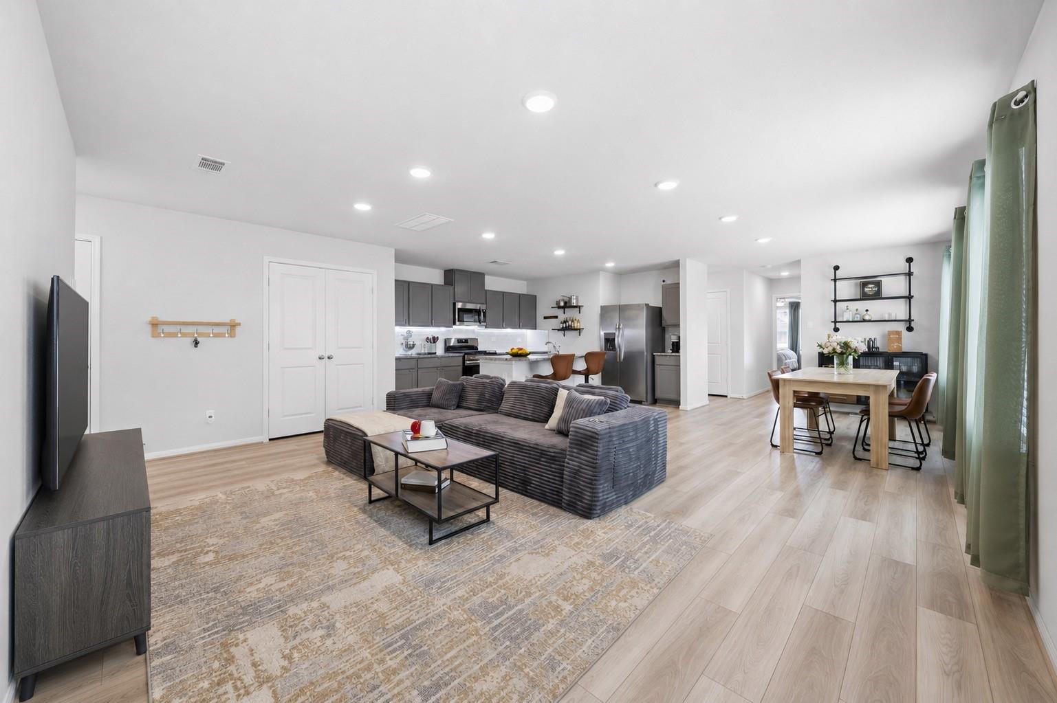 Open-plan living and dining area with a gray sectional, light wood floors, and kitchen beyond.