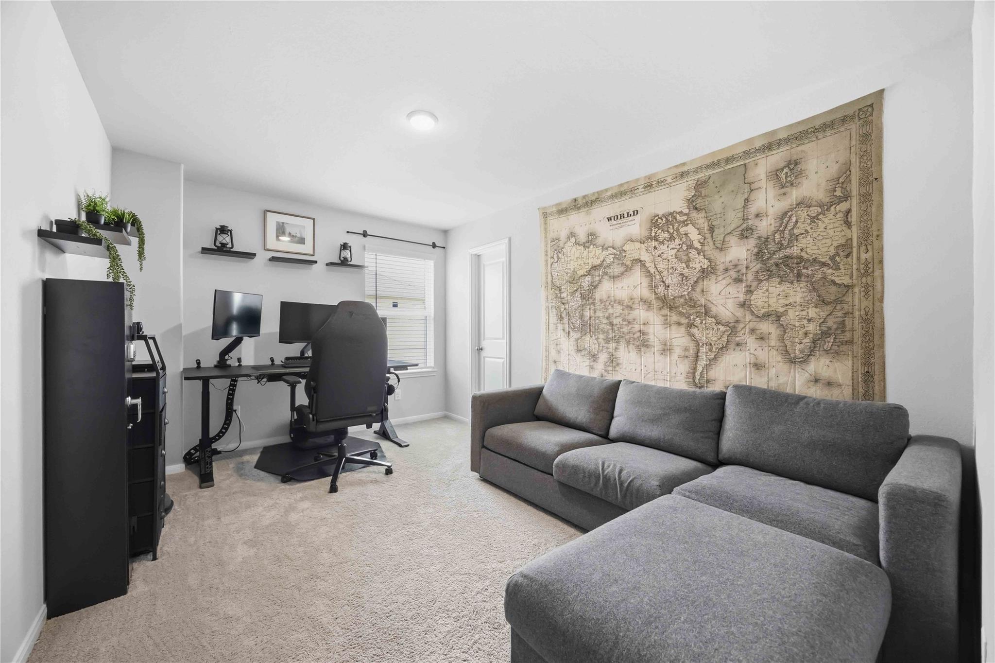 Home office and lounge with a dual-monitor desk, gray sectional sofa, and oversized world map mural.