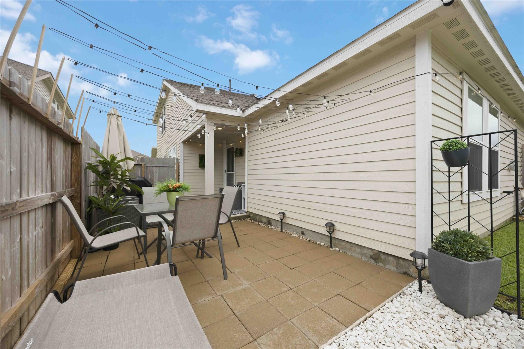 Backyard patio with outdoor seating, potted plants, privacy fencing, and overhead string lights.