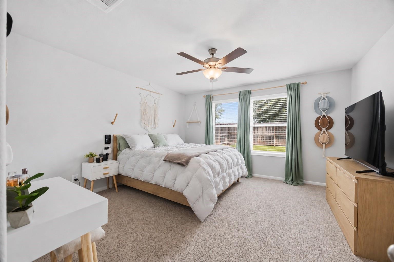 Furnished bedroom with a white bed, sage green curtains, and a ceiling fan.