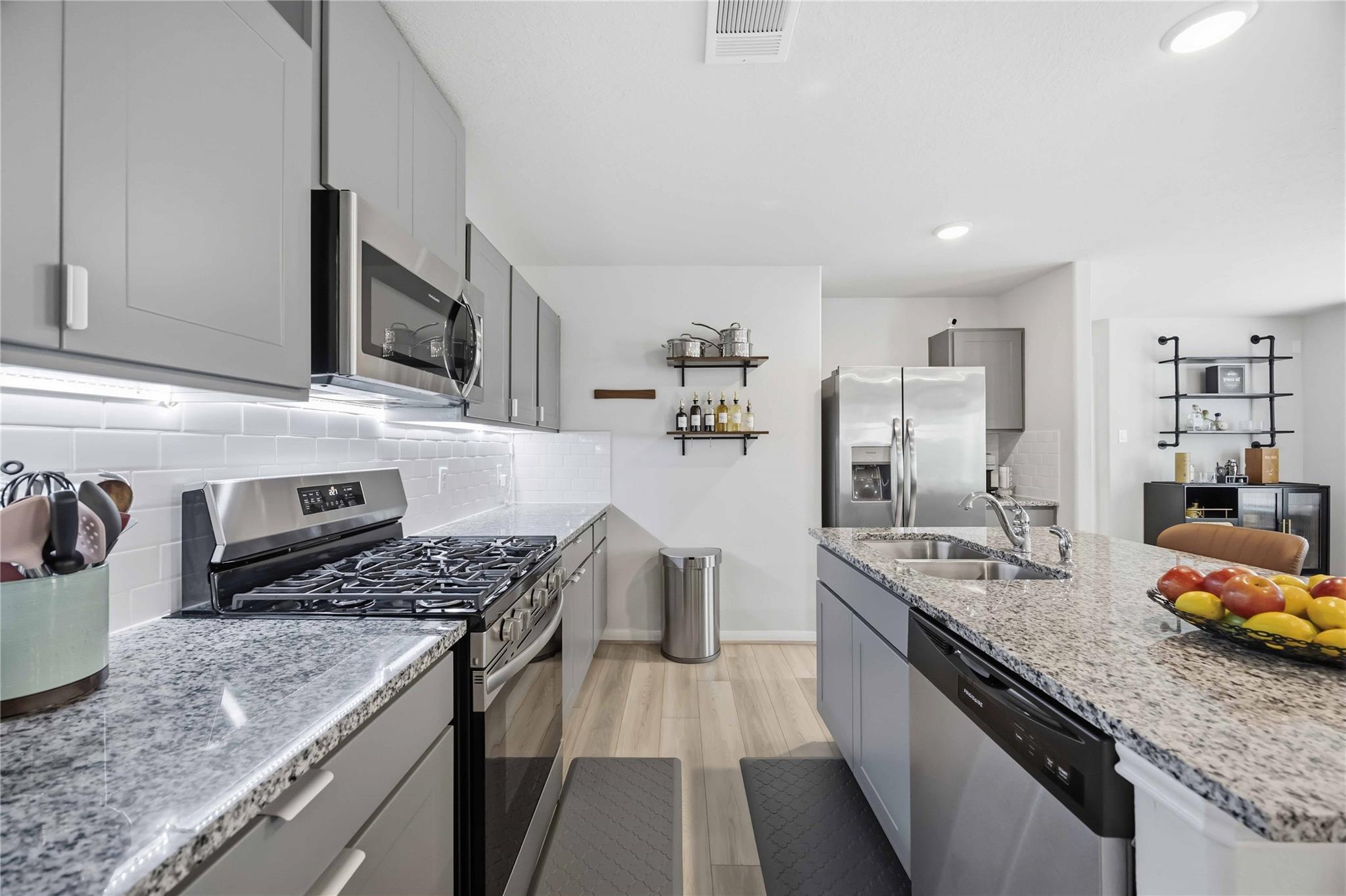 Modern kitchen with gray cabinets, granite counters, stainless appliances, and a large island with double sink.