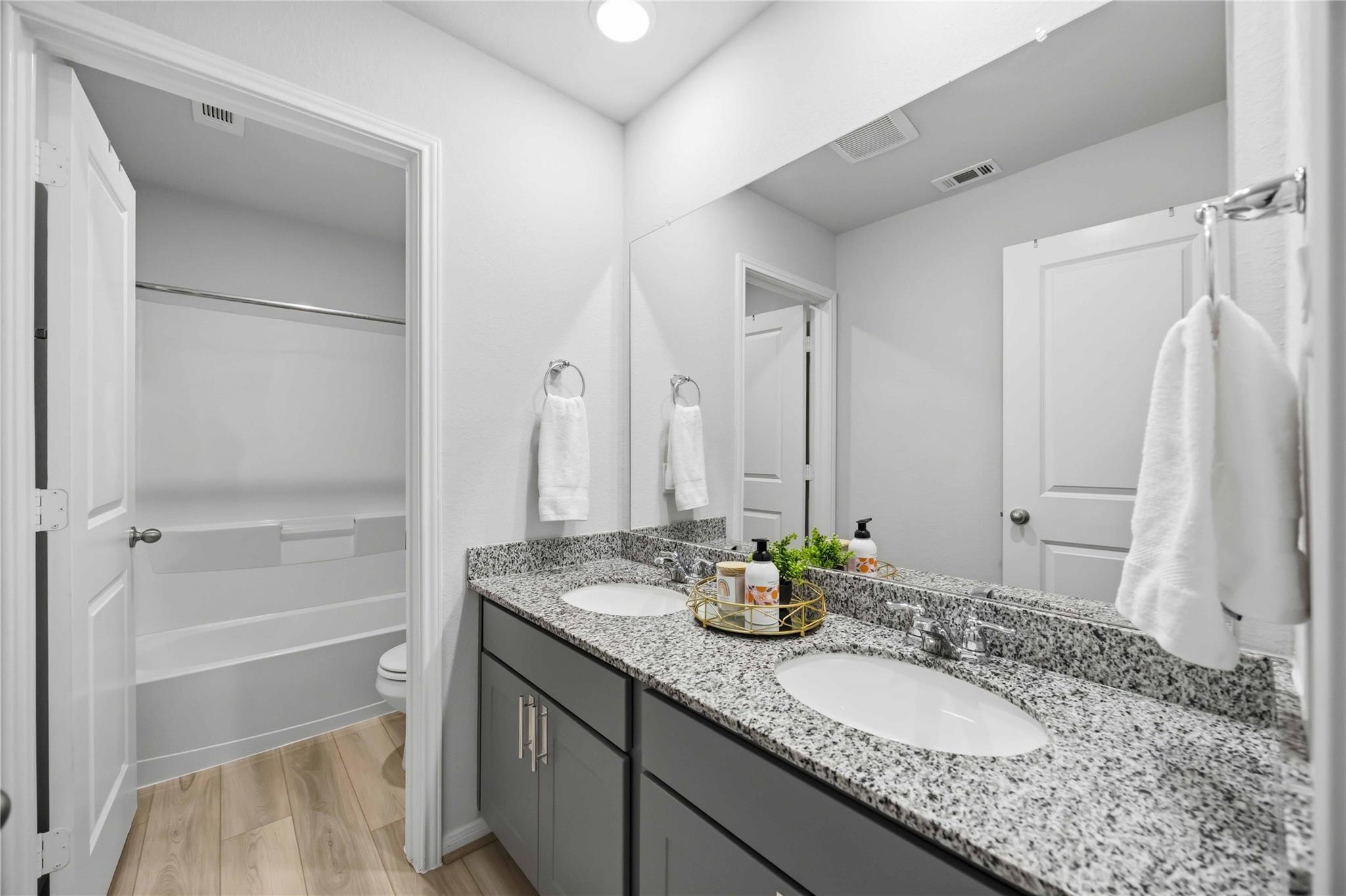 Bathroom with a granite double-sink vanity and an open doorway to a separate toilet area.