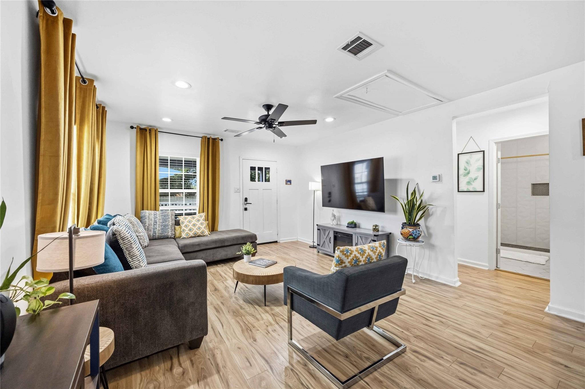Living room with a gray sectional, mustard curtains, wood-look floors, and a wall-mounted television.