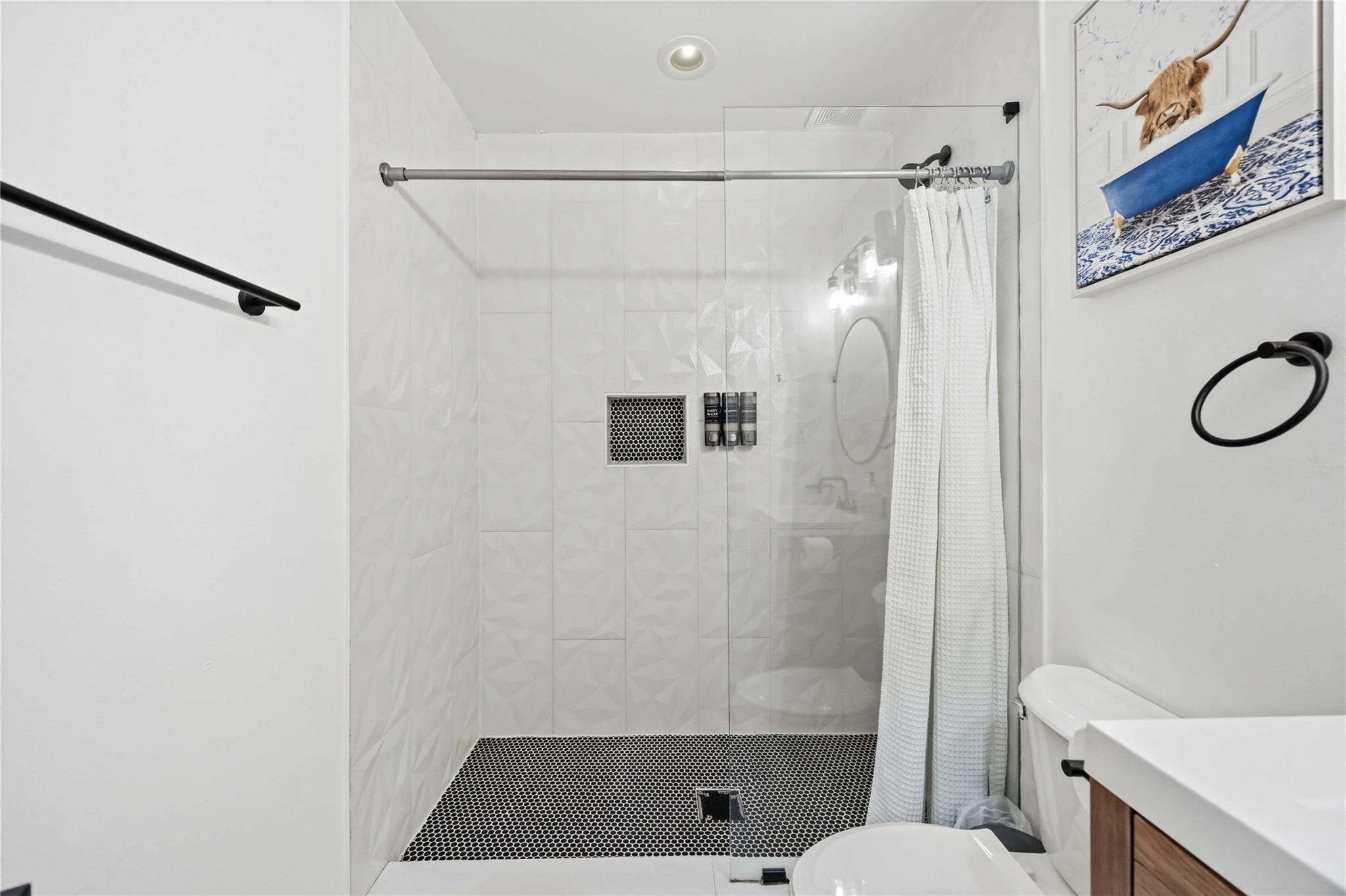 Modern bathroom with a spacious walk-in shower, geometric white tile, and black mosaic floor.