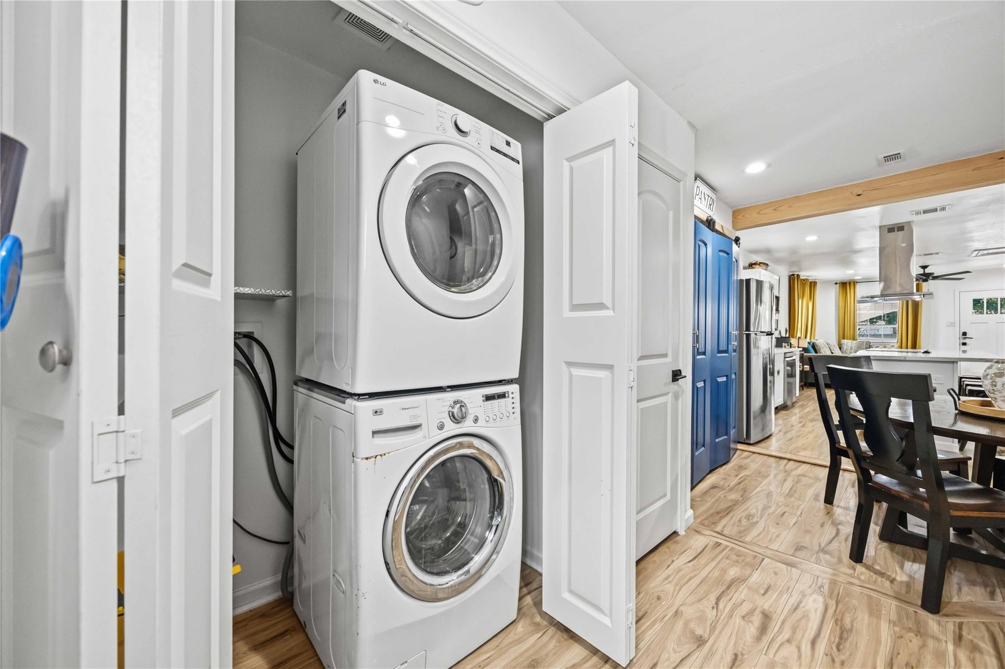 Laundry closet with stacked front-loading washer and dryer beside a kitchen with blue pantry doors.