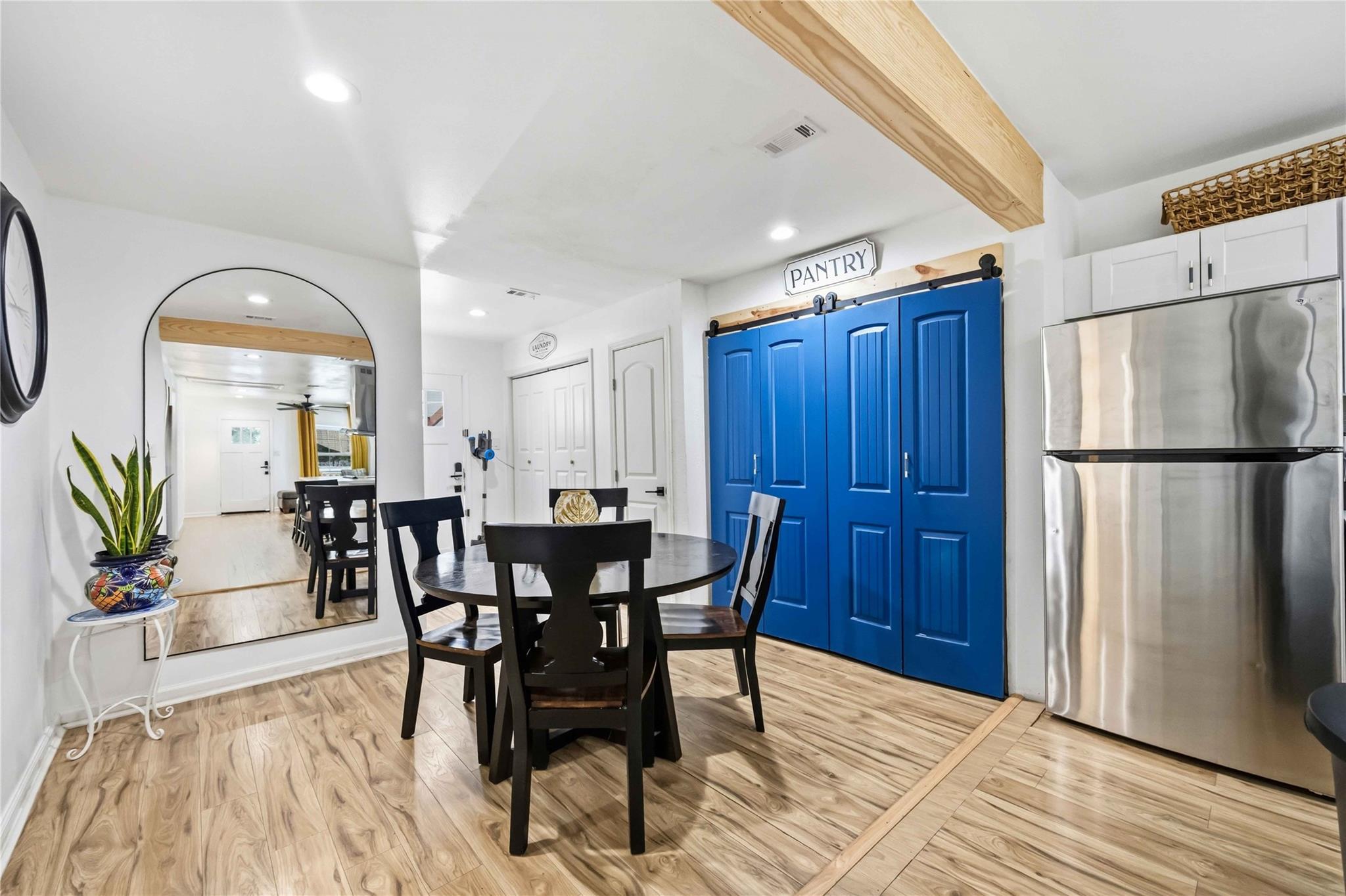 Dining area with blue pantry doors, a black round table, and stainless-steel refrigerator.