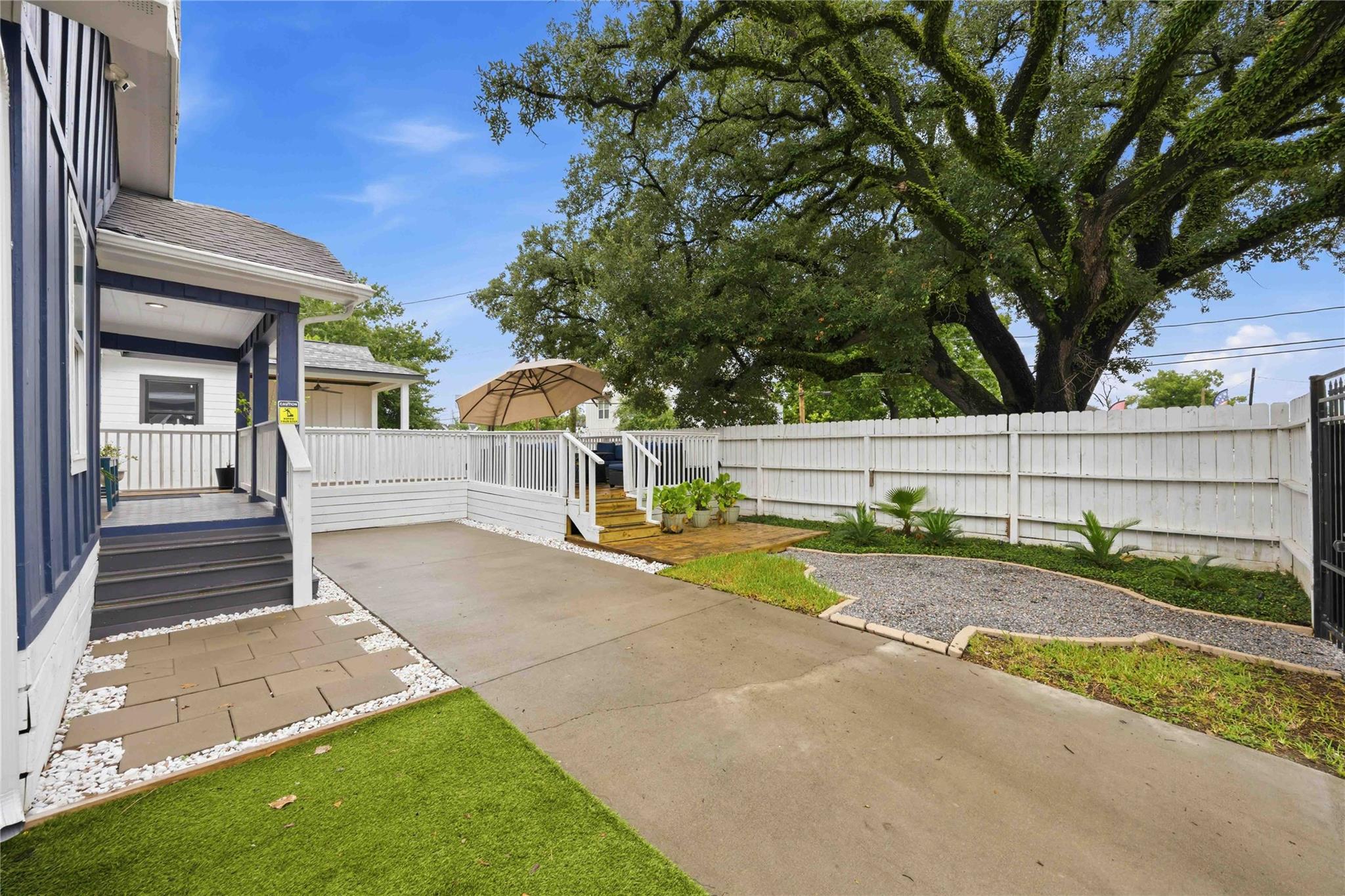 Fenced backyard patio with a raised deck, outdoor seating, and a large shade tree.