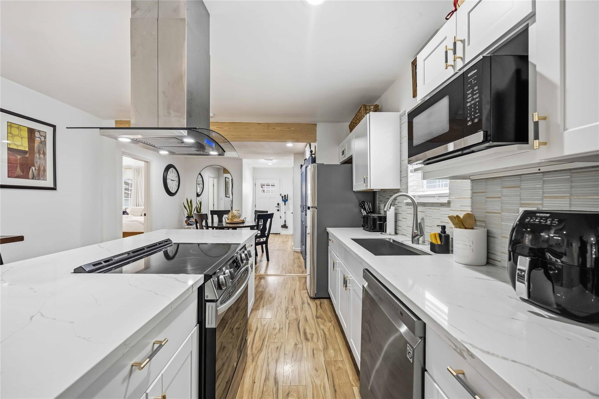 Renovated galley kitchen with white cabinets, marble-look counters, stainless appliances, and wood-look floors.