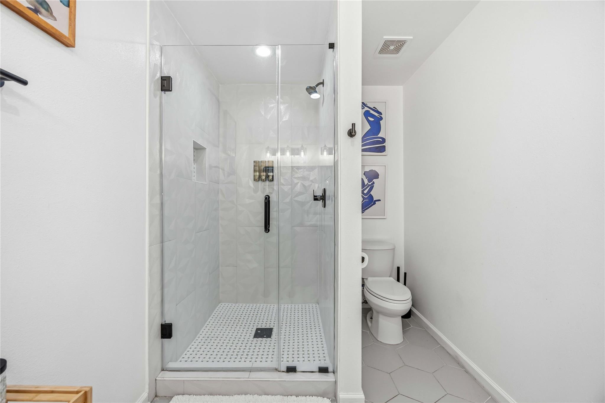 Bathroom with a glass-enclosed walk-in shower, geometric tile, black fixtures, and a toilet.