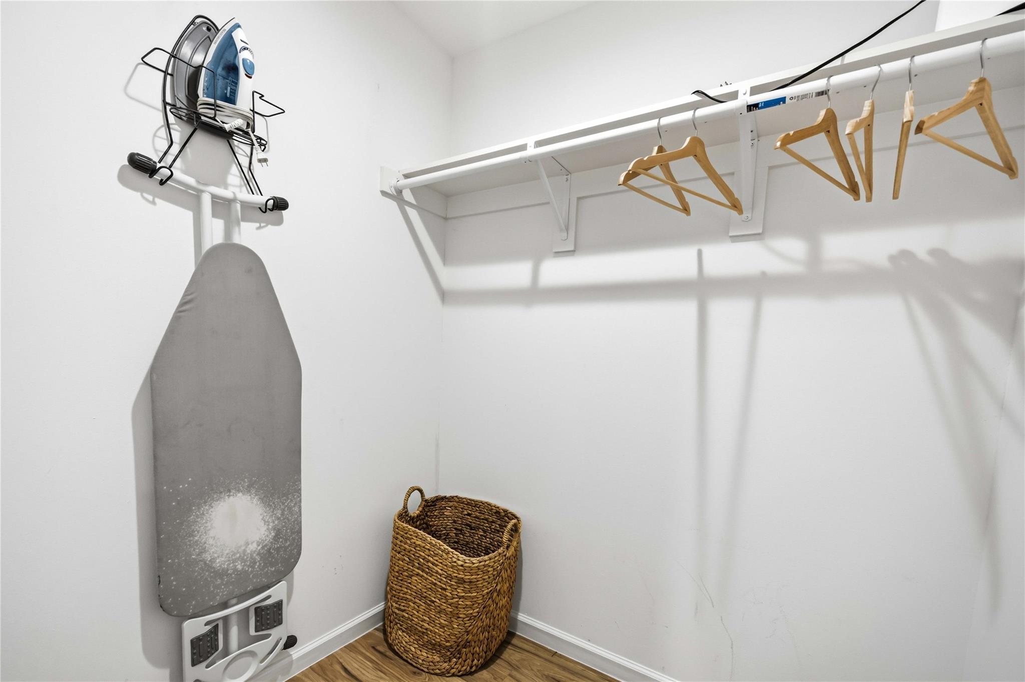 Laundry closet with a wall-mounted ironing board, wooden hangers, and a woven basket.