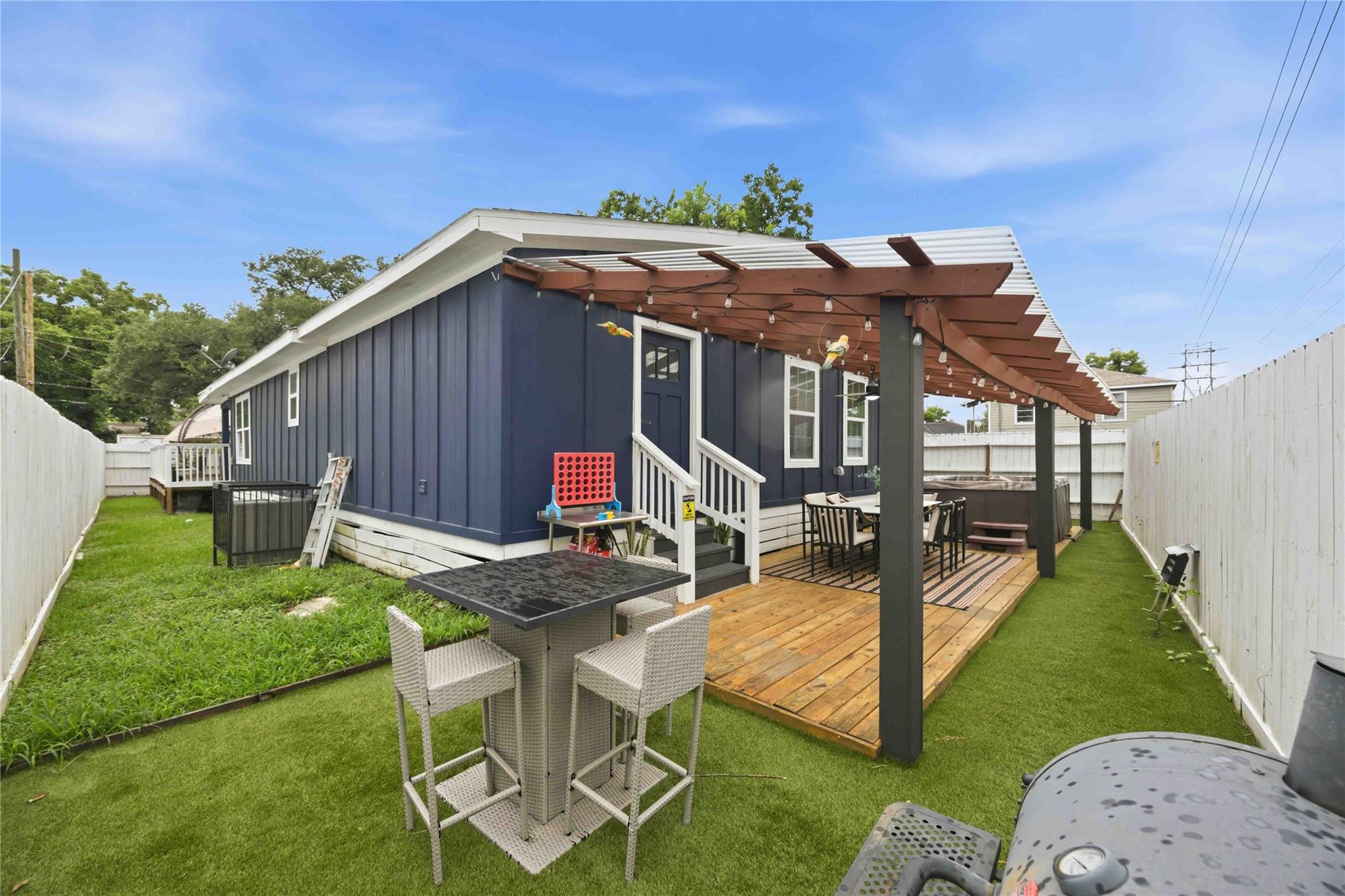 Backyard with a pergola-covered deck, outdoor dining set, and fenced lawn.