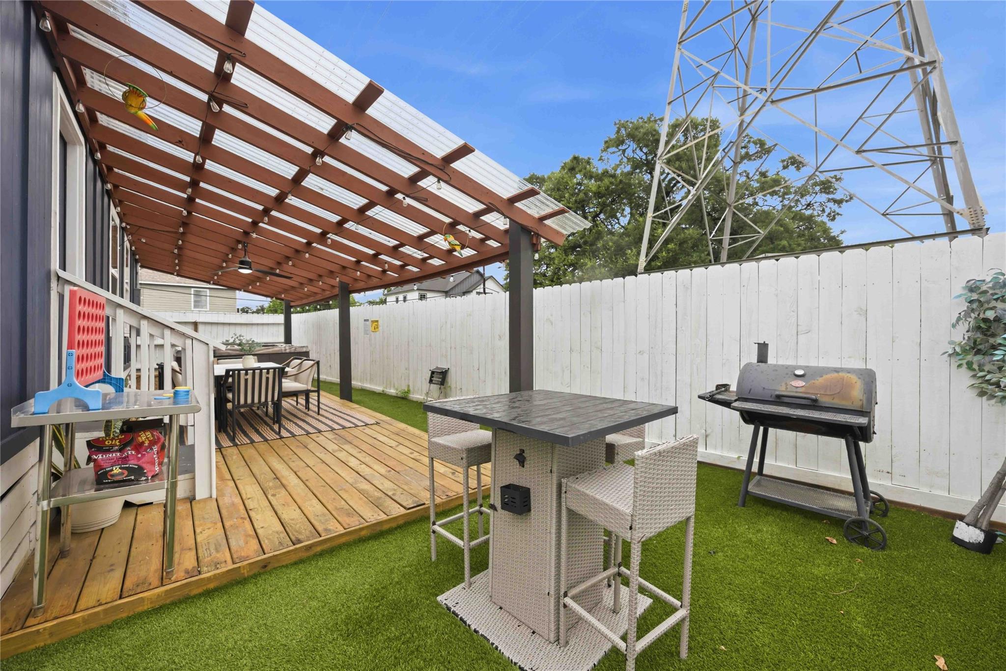 Backyard deck beneath a pergola, with outdoor dining furniture, artificial turf, and a barbecue grill.