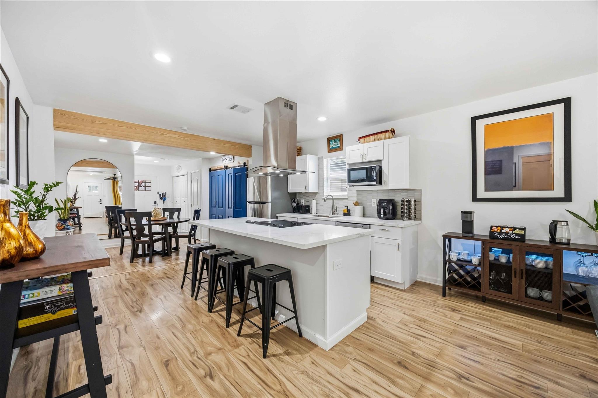 Kitchen with a large white island, black stools, stainless steel range hood, and blue pantry doors.