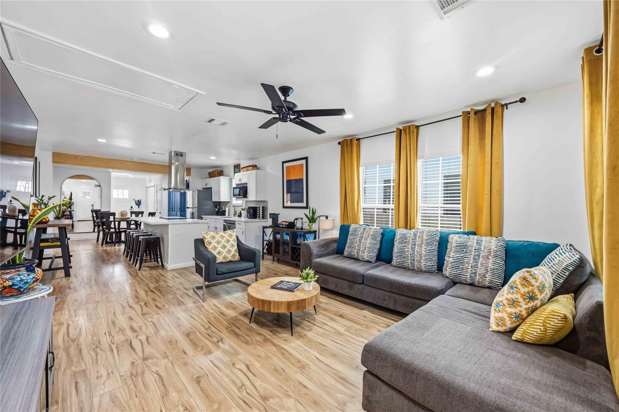 Open-plan living room and kitchen with a gray sectional, mustard curtains, and island seating.