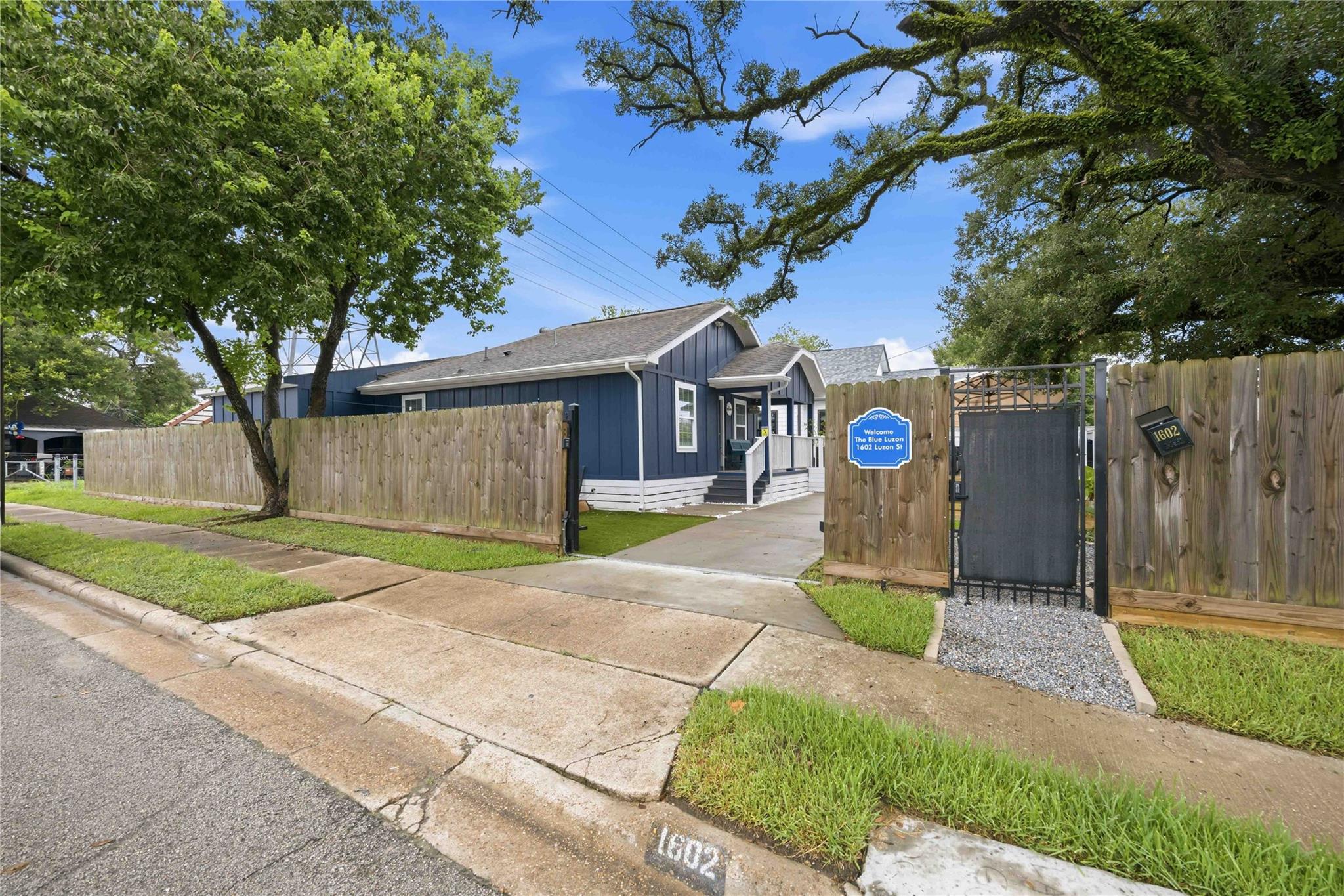 Blue single-story home behind a wooden fence, with a black gate and a sign welcoming visitors to The Blue Luzon.