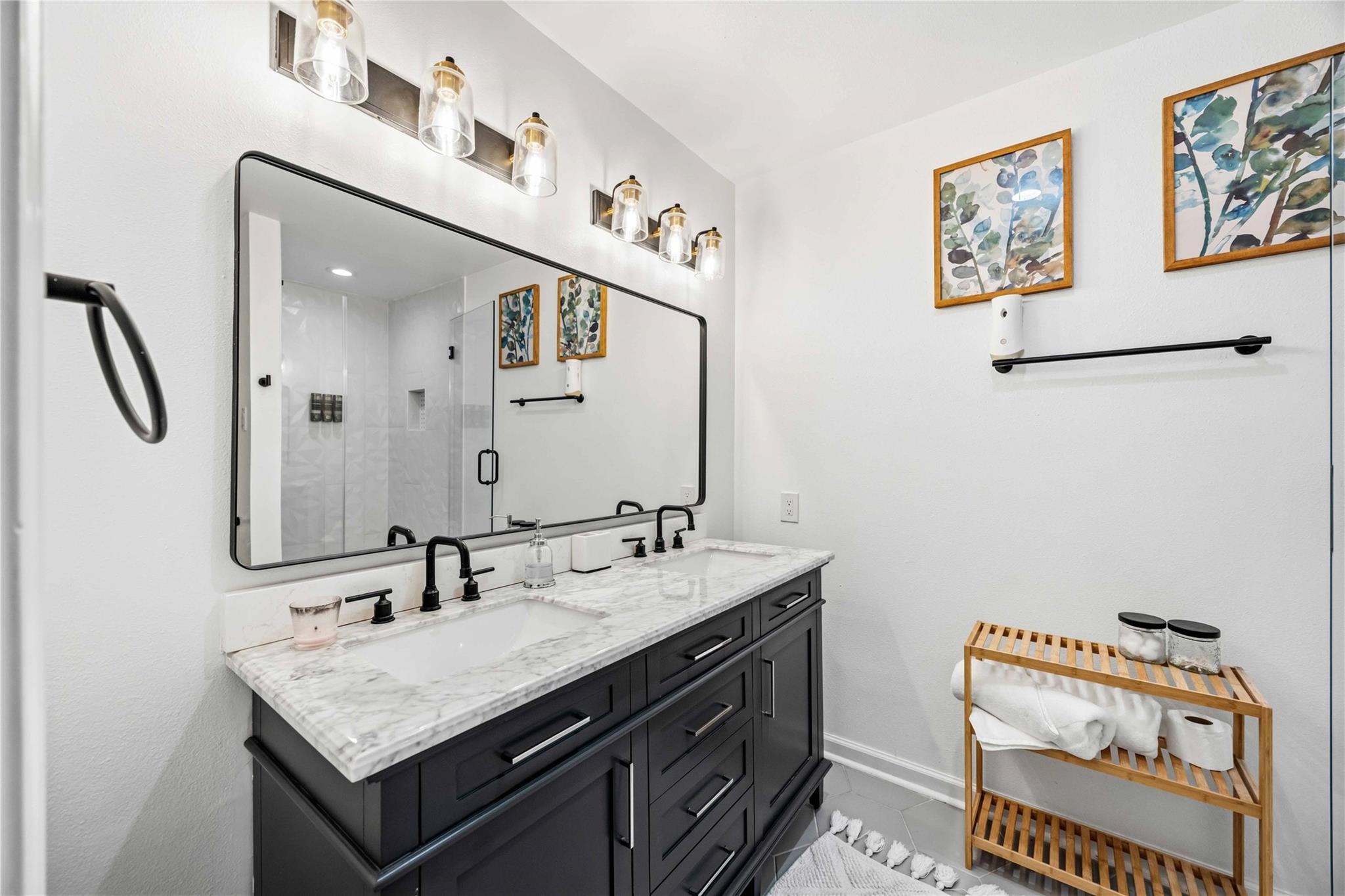 Bathroom with dark vanity, marble countertop, large mirror, and glass-enclosed shower.