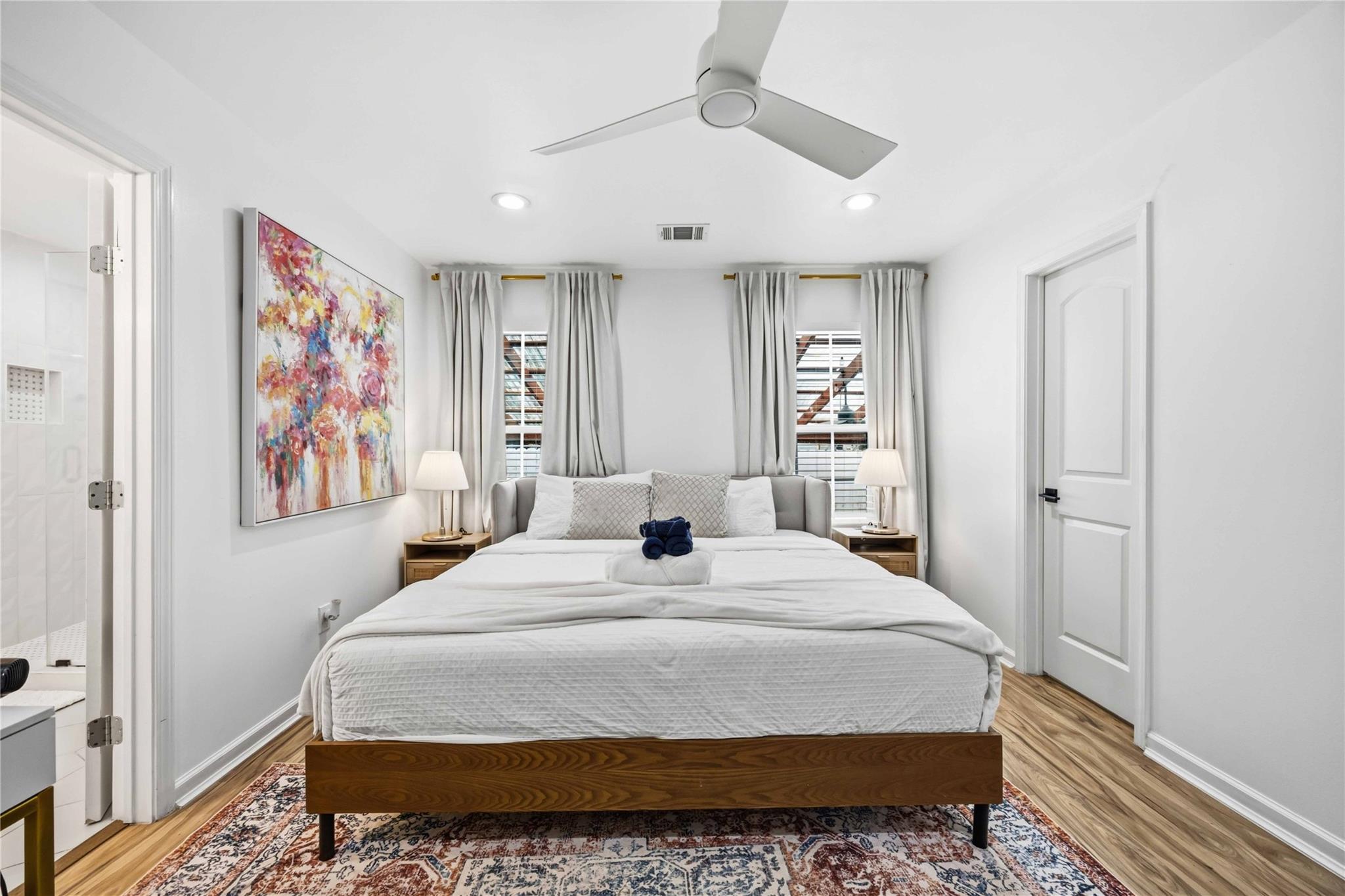 Staged bedroom with a wooden bed, colorful abstract artwork, and an open doorway to the bathroom.
