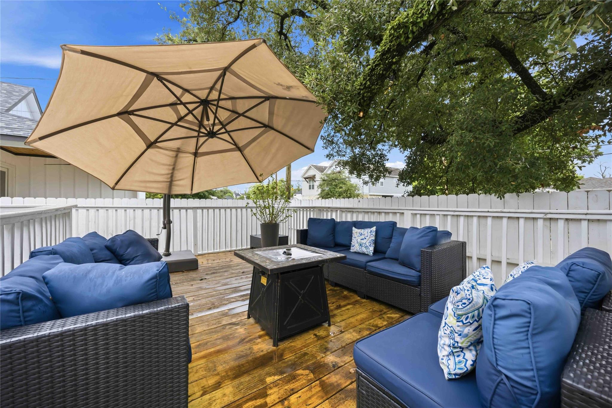 Deck with blue-cushioned wicker seating, a large umbrella, and white privacy fence.