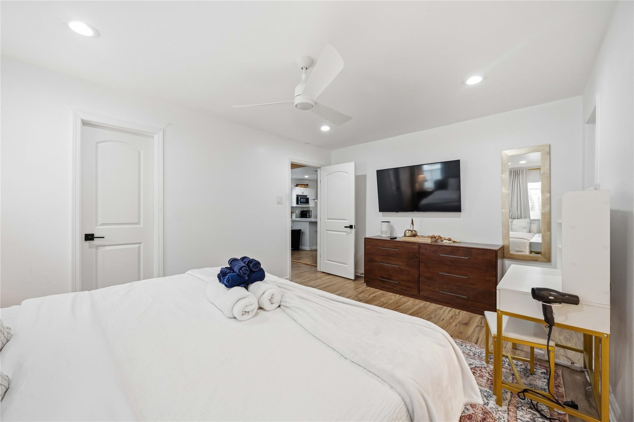 Bedroom with a white bed, rolled towels, wall-mounted TV, and dark wood dresser.
