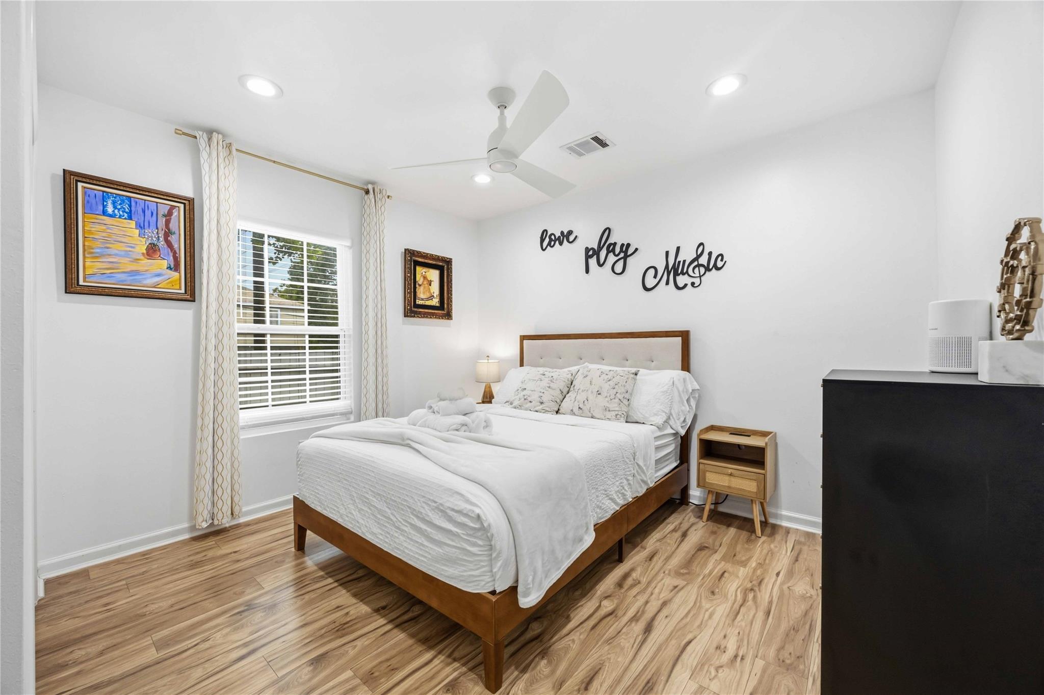 Bedroom with a wooden bed, white linens, wood-look flooring, and “love play music” lettering above the headboard.