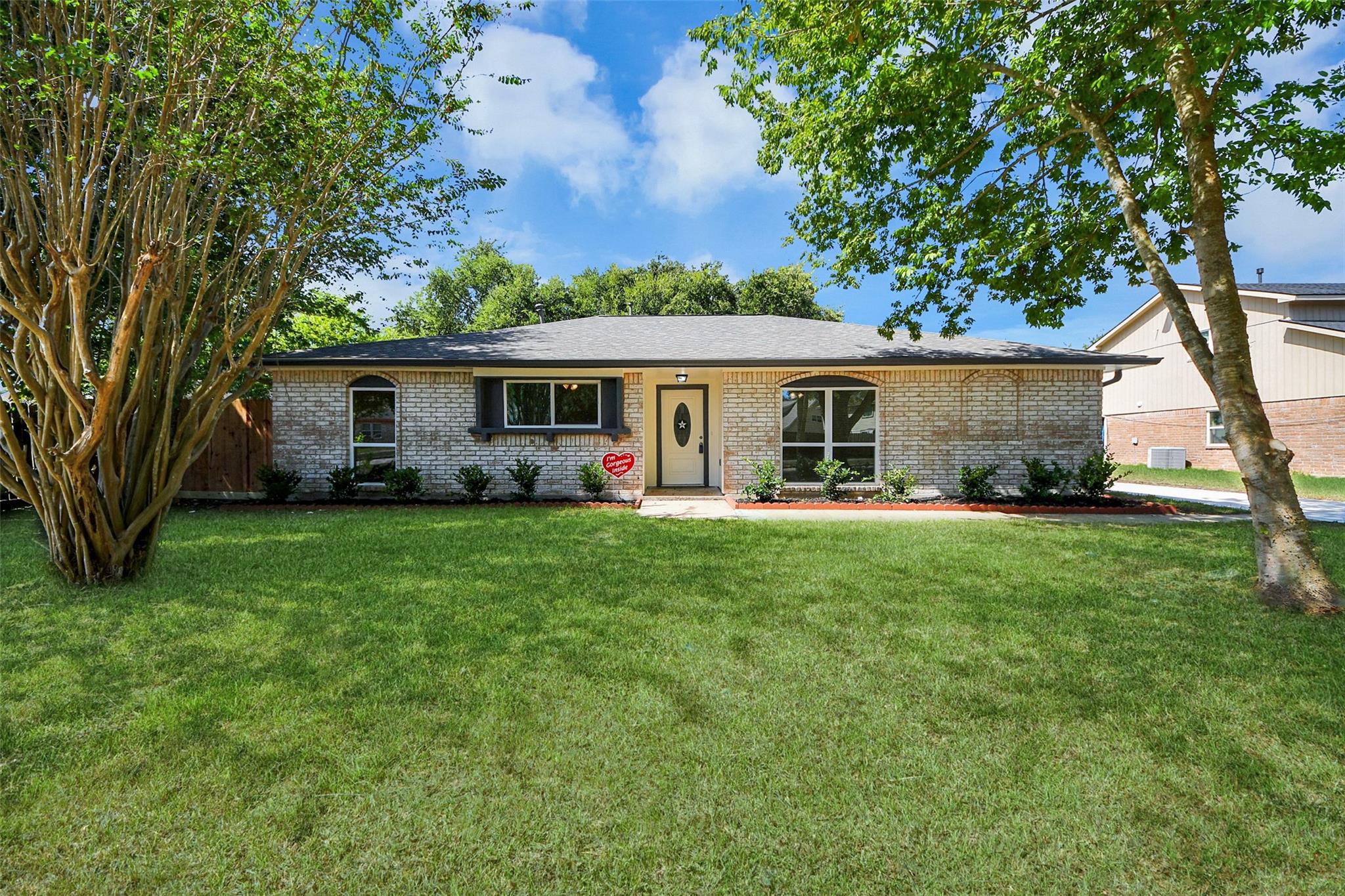 Single-story brick house with a centered entry, broad green lawn, and mature trees.