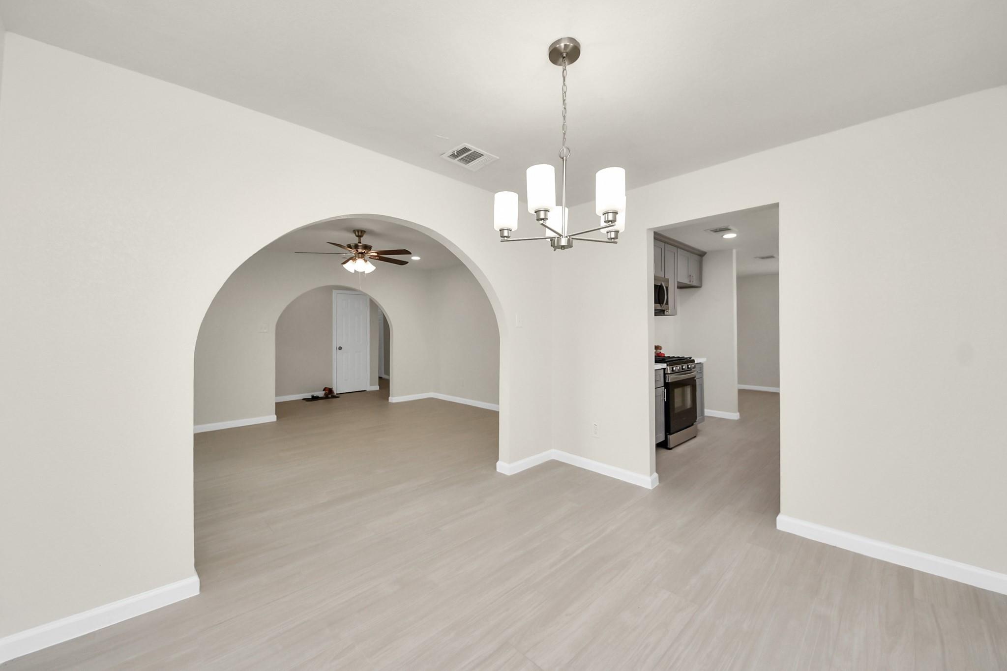 Empty dining area with a modern chandelier and wide arched opening to an adjoining room.