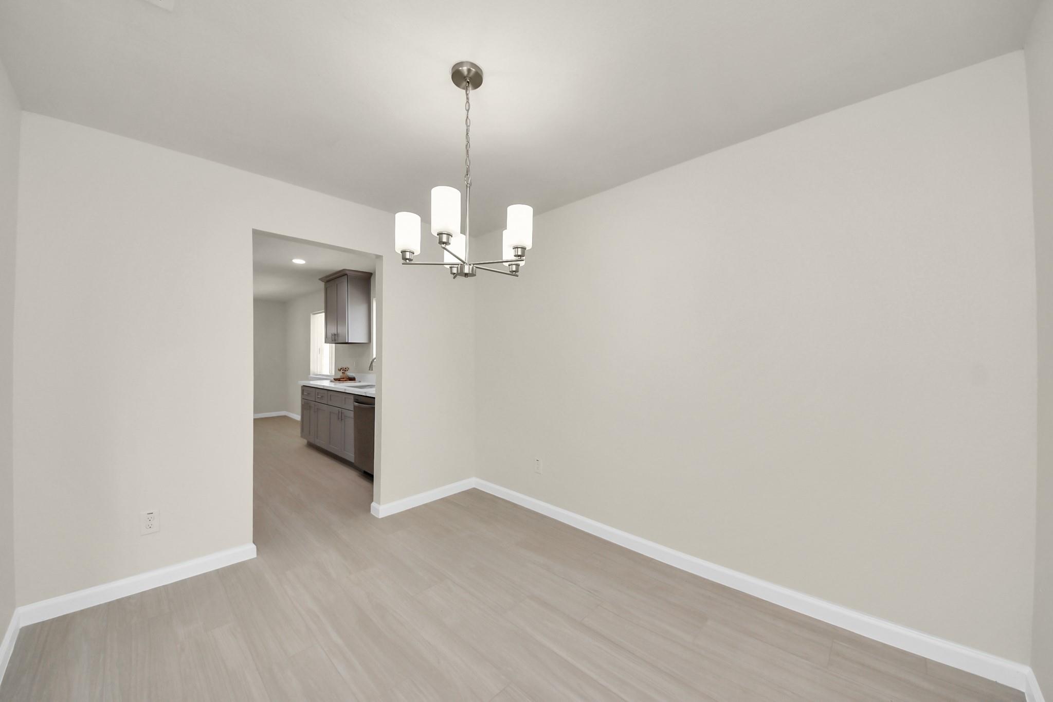 Unfurnished dining area with a modern chandelier and a view through to the kitchen.