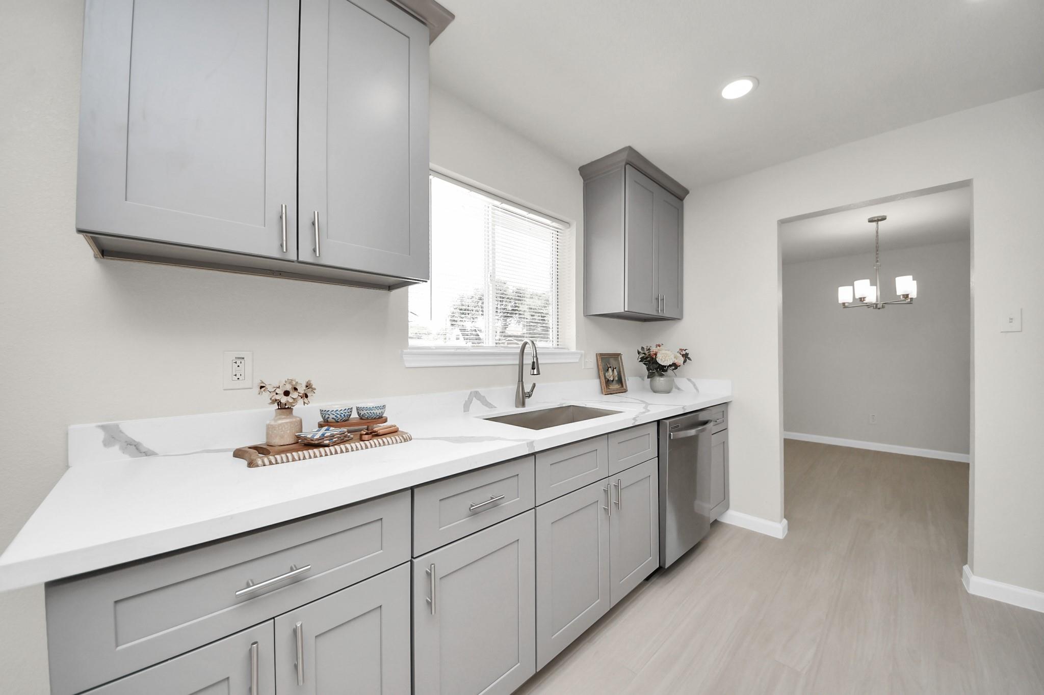 Kitchen with gray shaker cabinets, veined quartz counters, and a sink beneath a window.