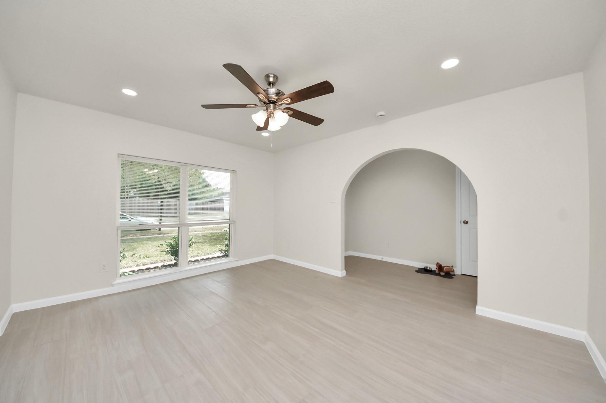 Empty room with pale flooring, a wide window, an arched opening, and a ceiling fan.